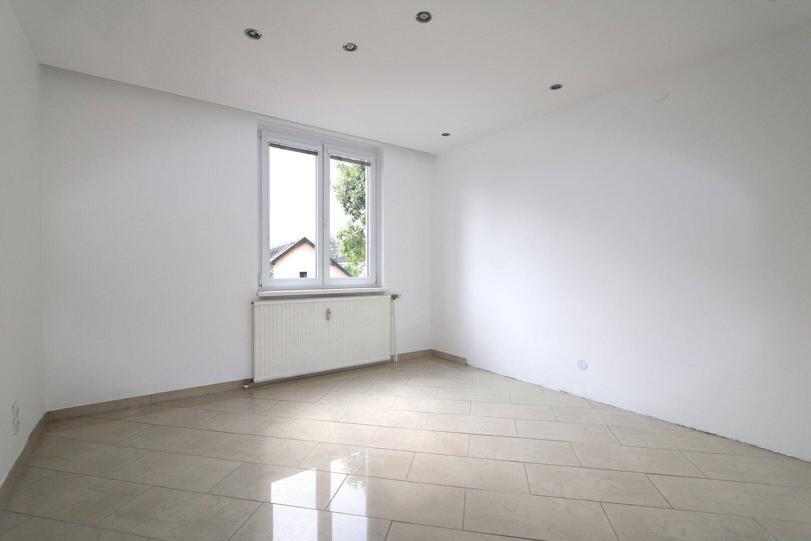 Leeres Schlafzimmer mit Fliesenboden, Einbaustrahlern und Fenster mit Ausblick.
