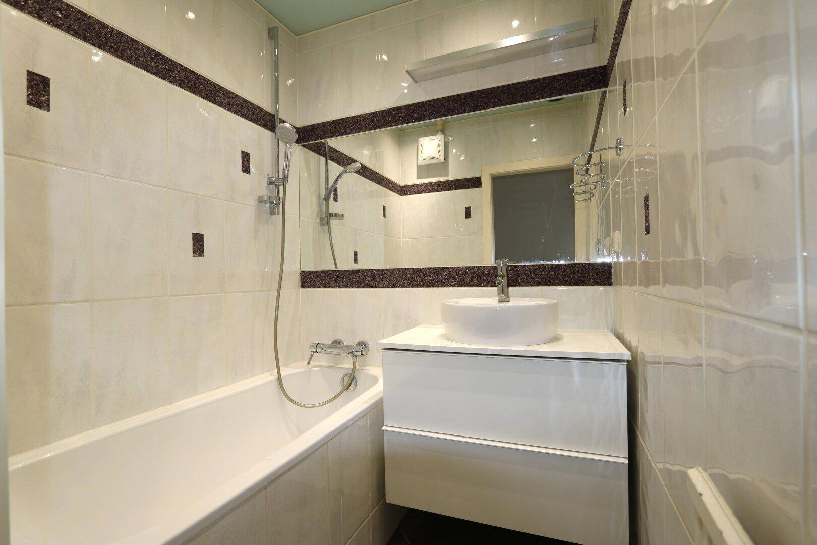 Modernes Badezimmer mit Badewanne, Waschbecken und großen Wandfliesen.