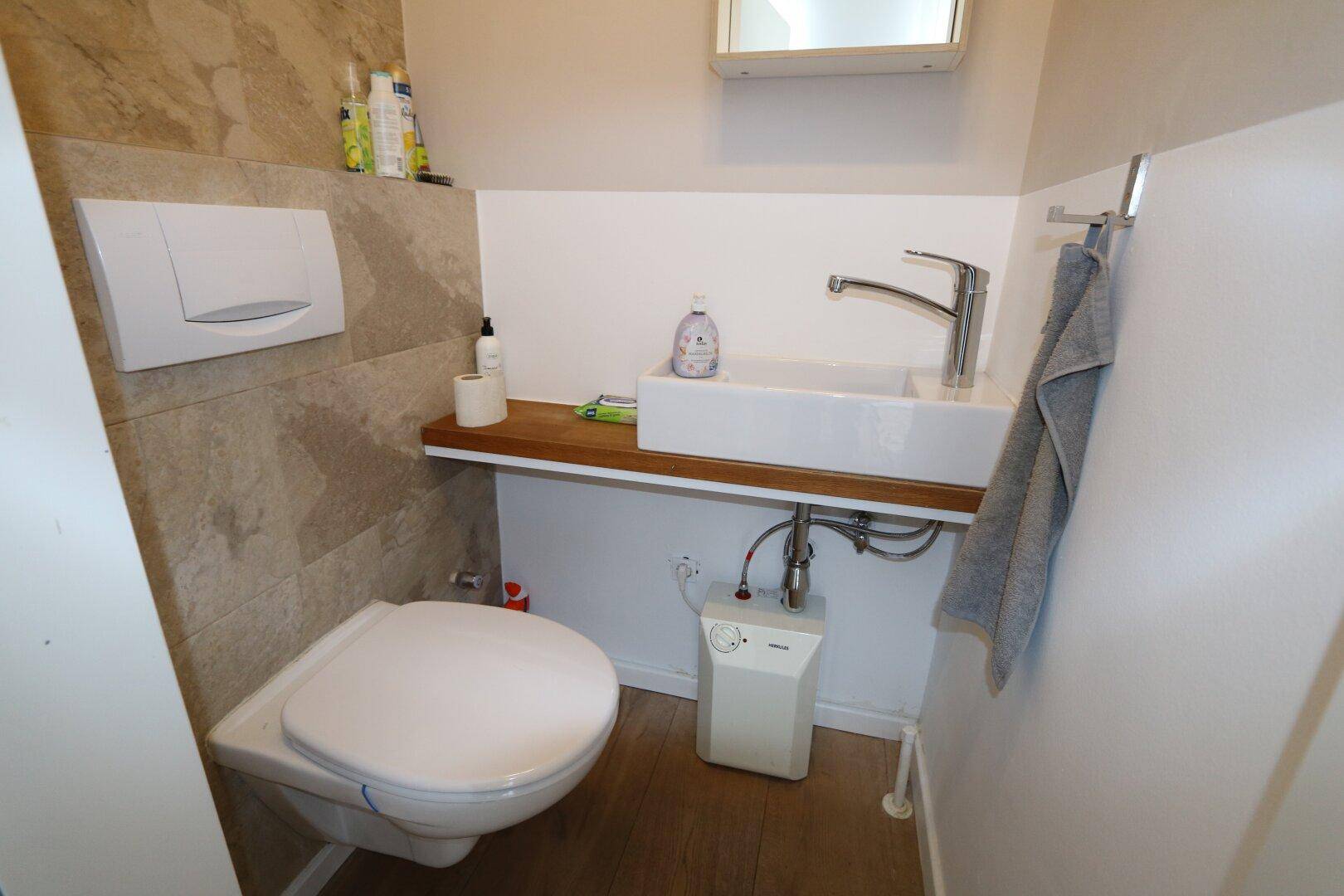 Modernes Gäste-WC mit Wand-WC, Aufsatzwaschbecken und gefliester Wand, ausgestattet mit hochwertigen Armaturen.