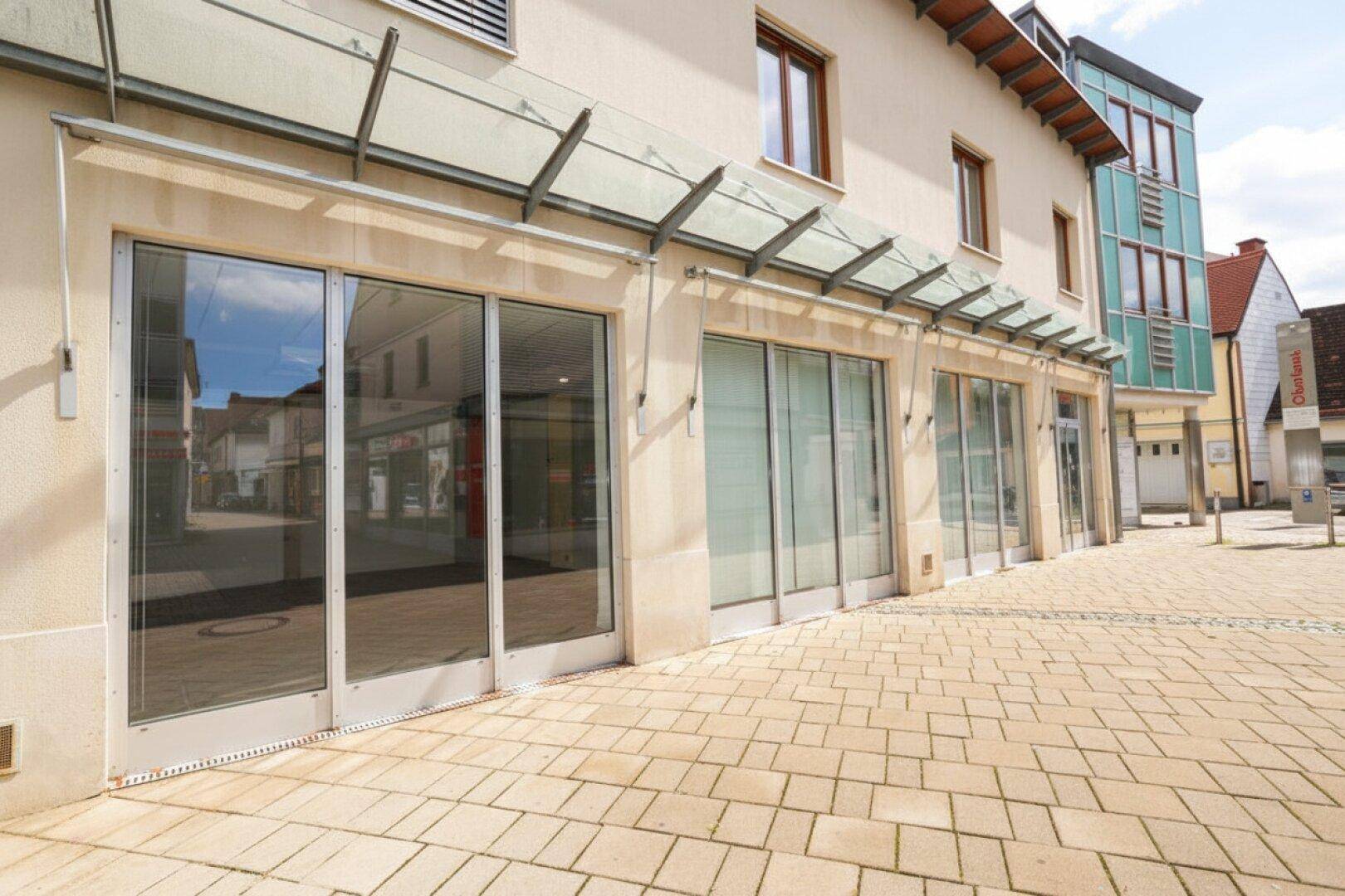 Moderne Geschäftsfassade mit großen Schaufenstern und einem gepflasterten Gehweg vor dem Gebäude, ideal für Einzelhandel.