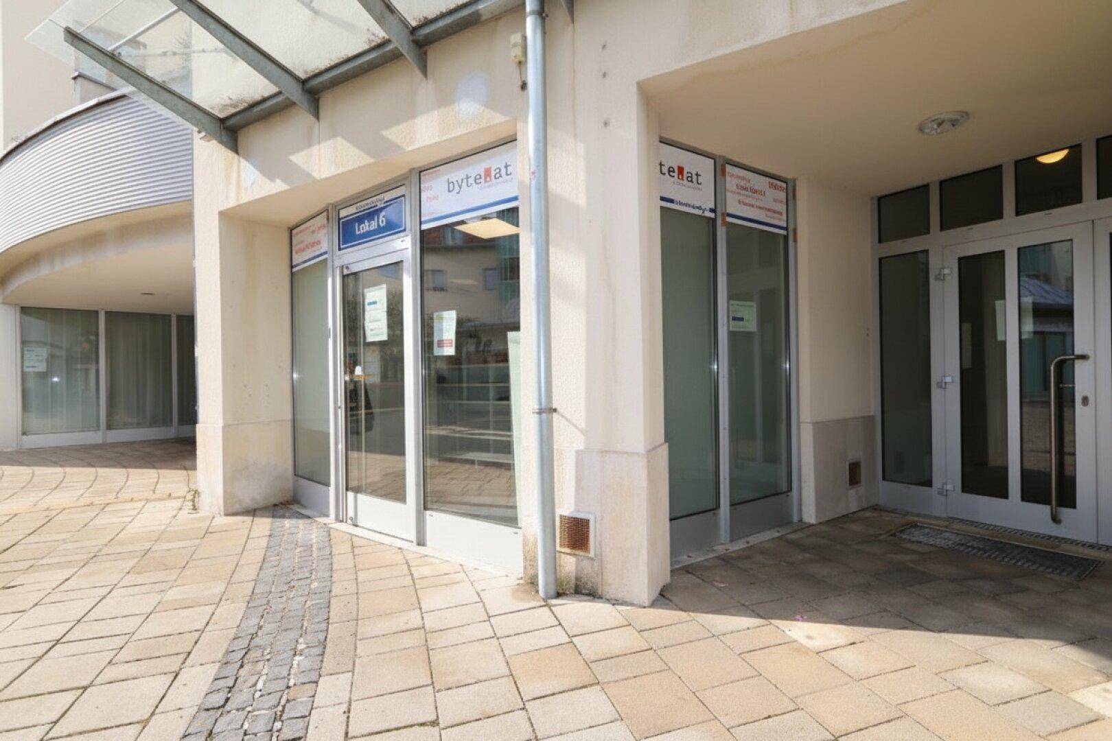 Eingangsbereich eines modernen Geschäftsgebäudes mit Glasfront und Überdachung, hell und zugänglich.