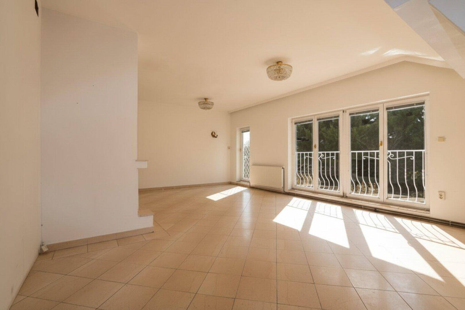 Helles Wohnzimmer im Dachgeschoss mit Fliesenboden und Zugang zum französischen Balkon.