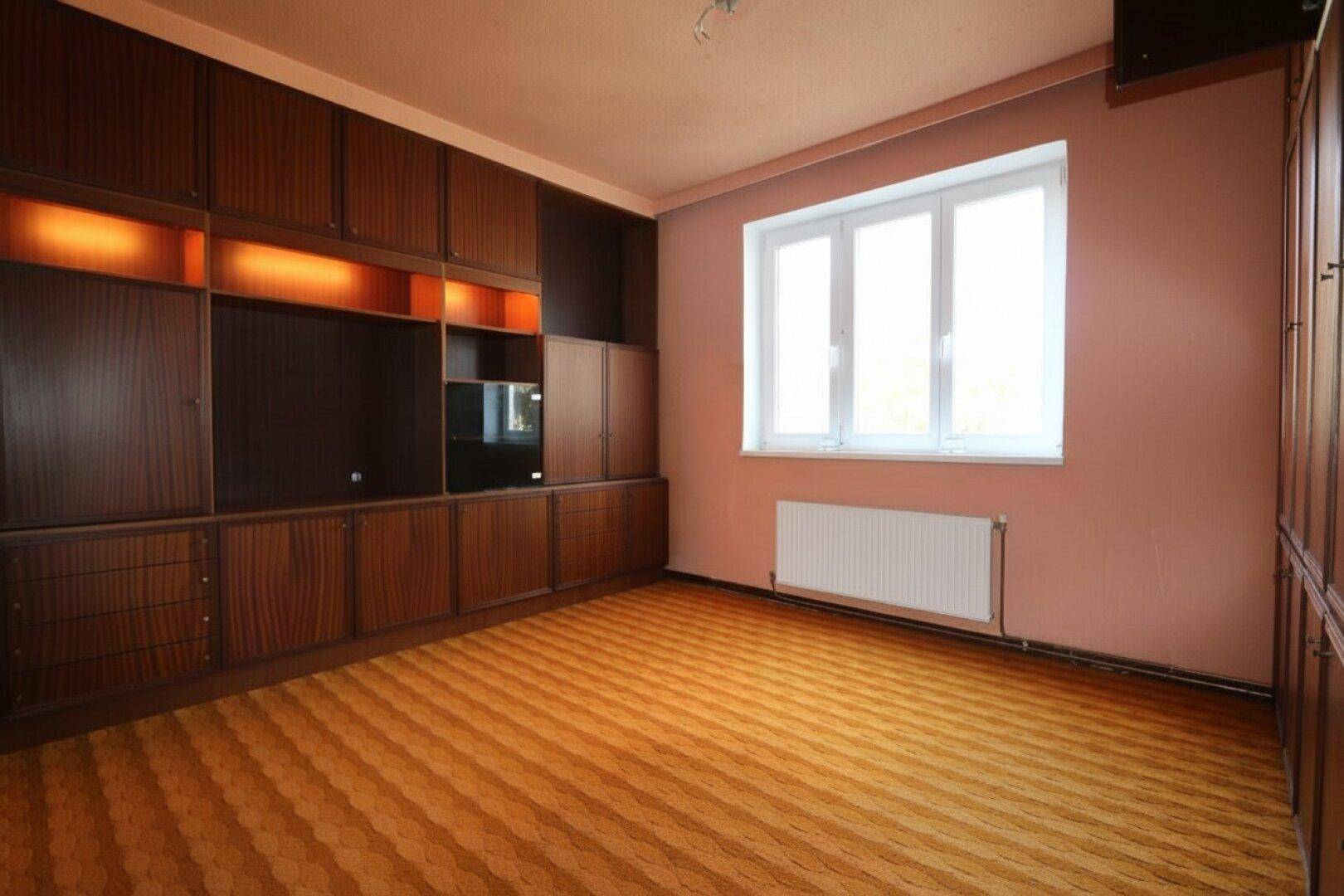 Geräumiger Raum mit Holzschrankwand und Fenster, ideal als Schlaf- oder Wohnzimmer.