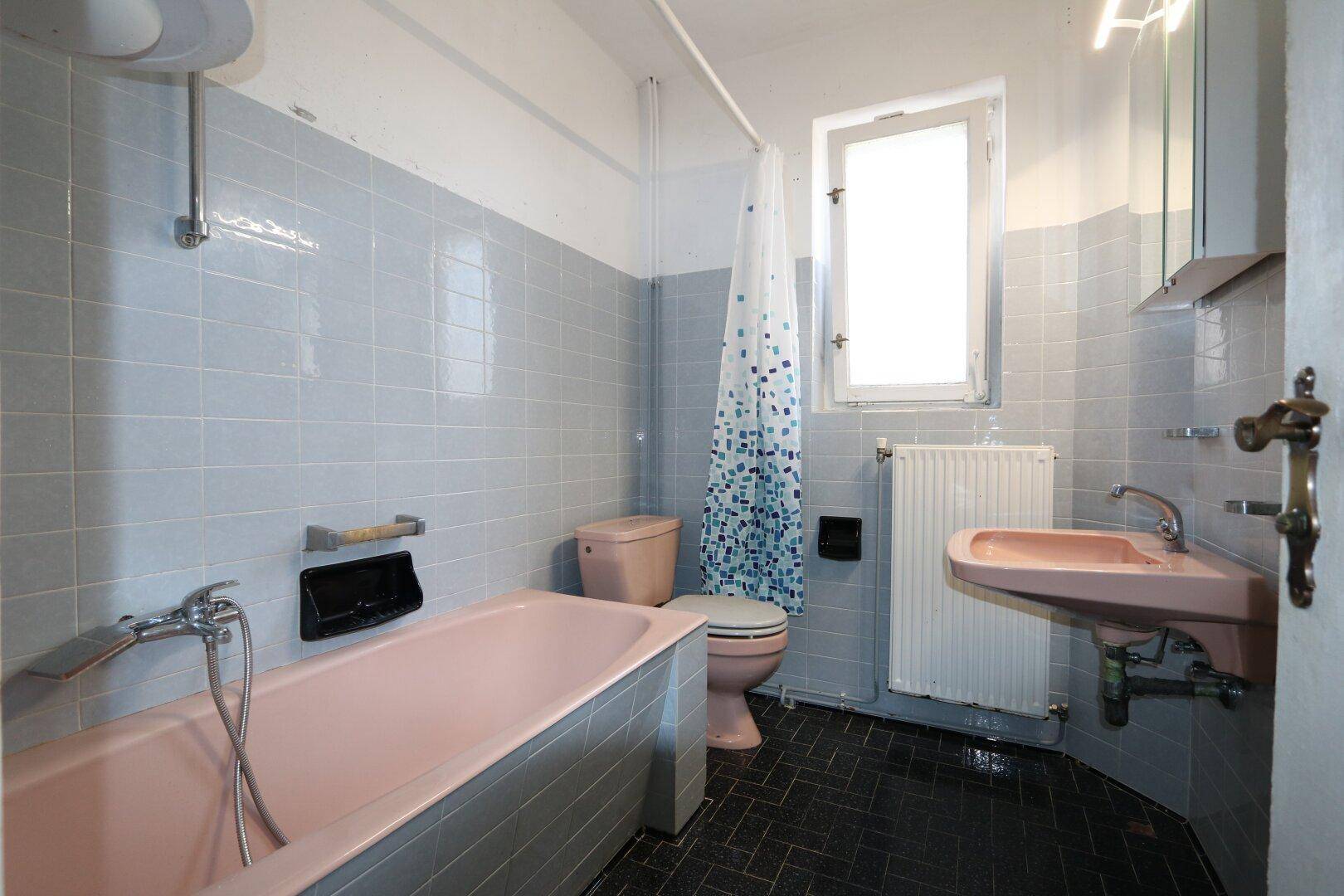 Badezimmer im Stil der 80er Jahre mit rosa Sanitärobjekten und blauen Fliesen.