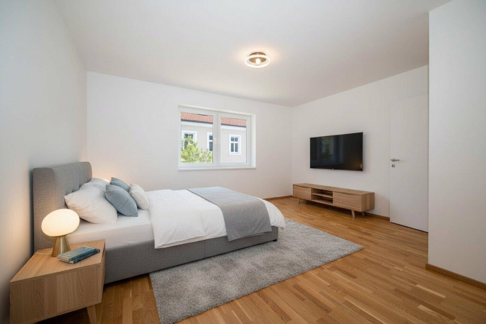 Modernes Schlafzimmer mit Holzboden, einem bequemen Bett und einem an der Wand montierten Fernseher.