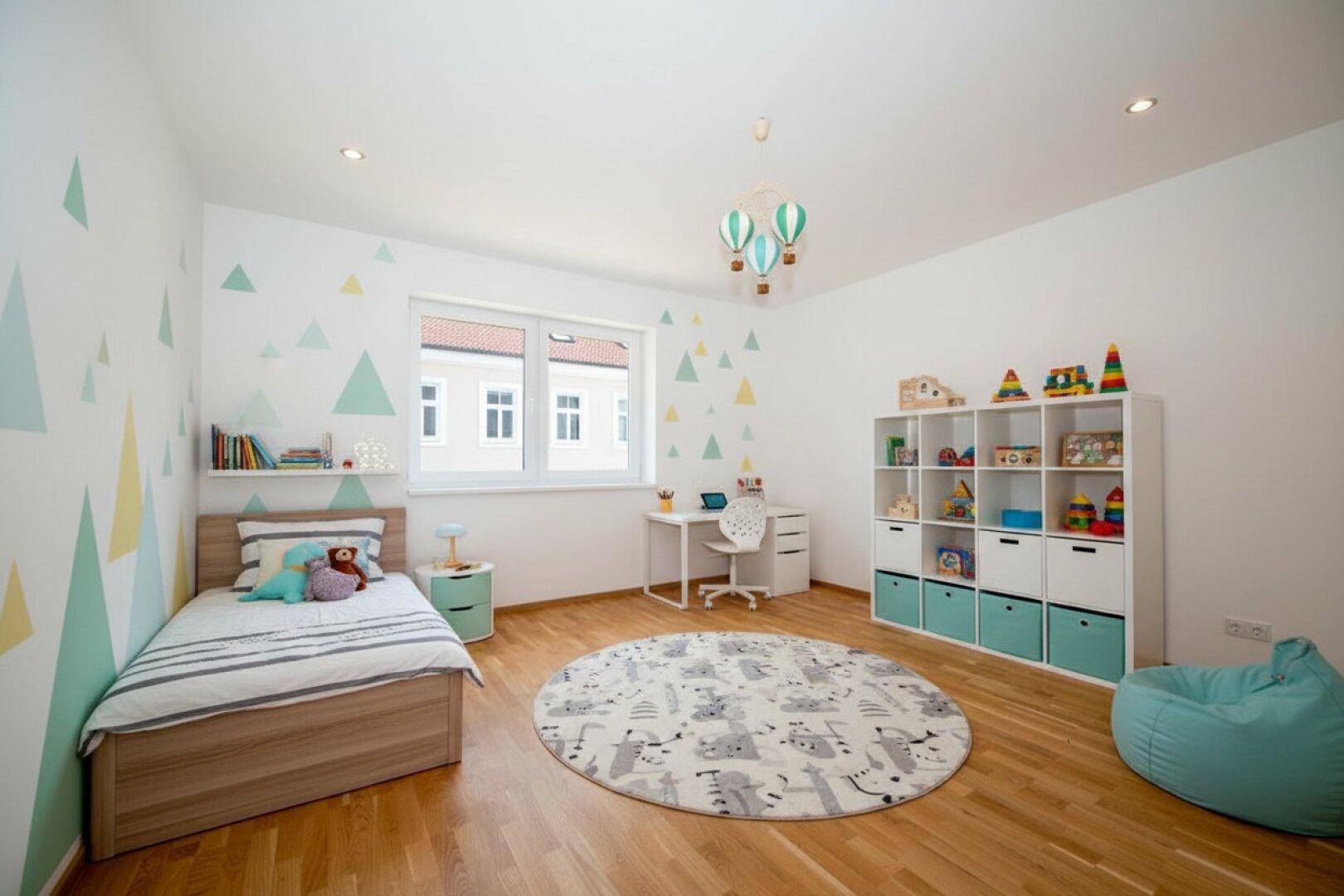 Freundliches Kinderzimmer mit Holzboden, farbigen Wanddekorationen und viel Stauraum für Spielzeug.