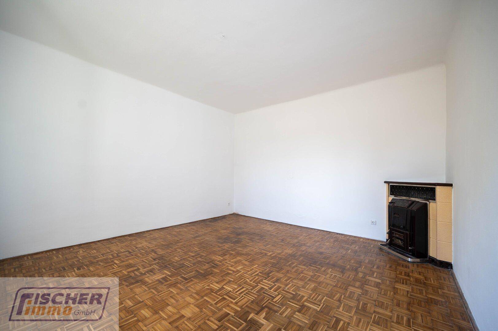 Geräumiges Zimmer mit Parkettboden und einem traditionellen Kaminofen in der Ecke.