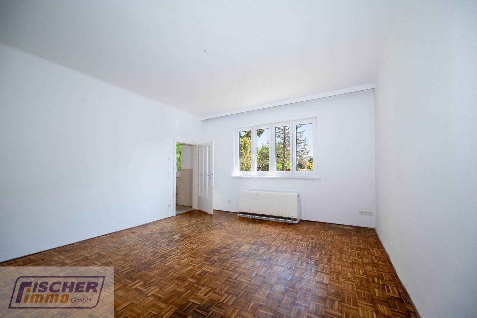Helles Zimmer mit Parkettboden, großem Fenster und Heizkörper unter der Fensterbank.