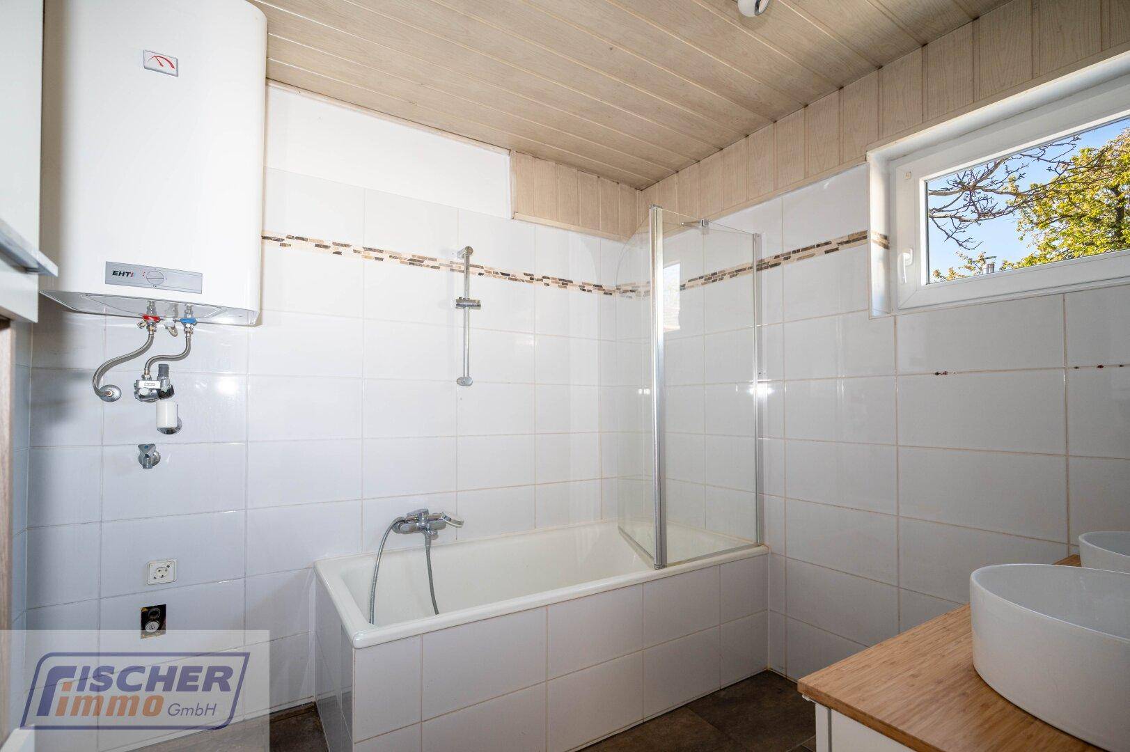 Badezimmer mit Badewanne, Duschvorrichtung, Boiler und Fenster für Tageslicht.