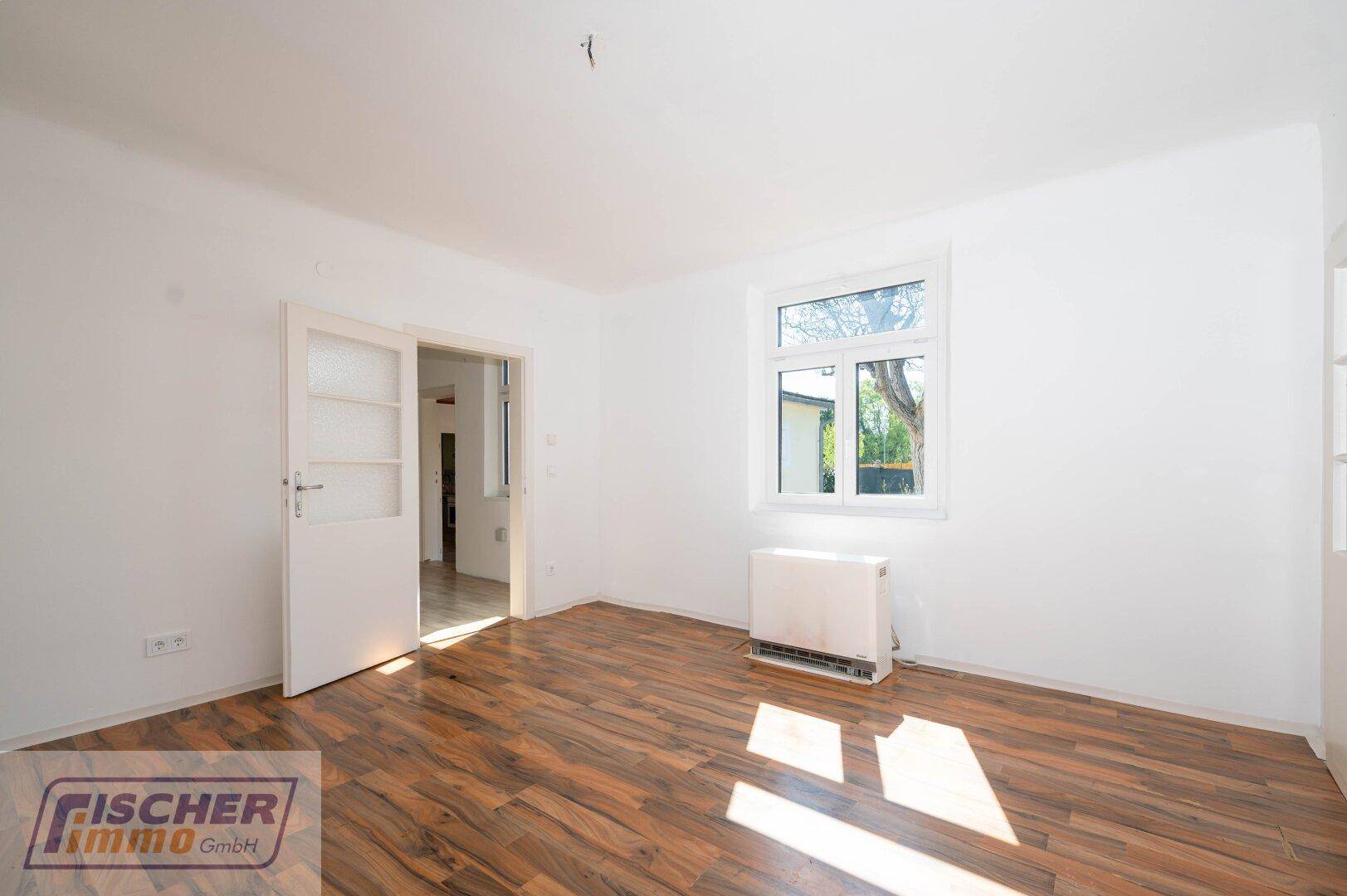 Geräumiges Zimmer mit Laminatboden, Fenster und Zugang zu einem weiteren Raum.