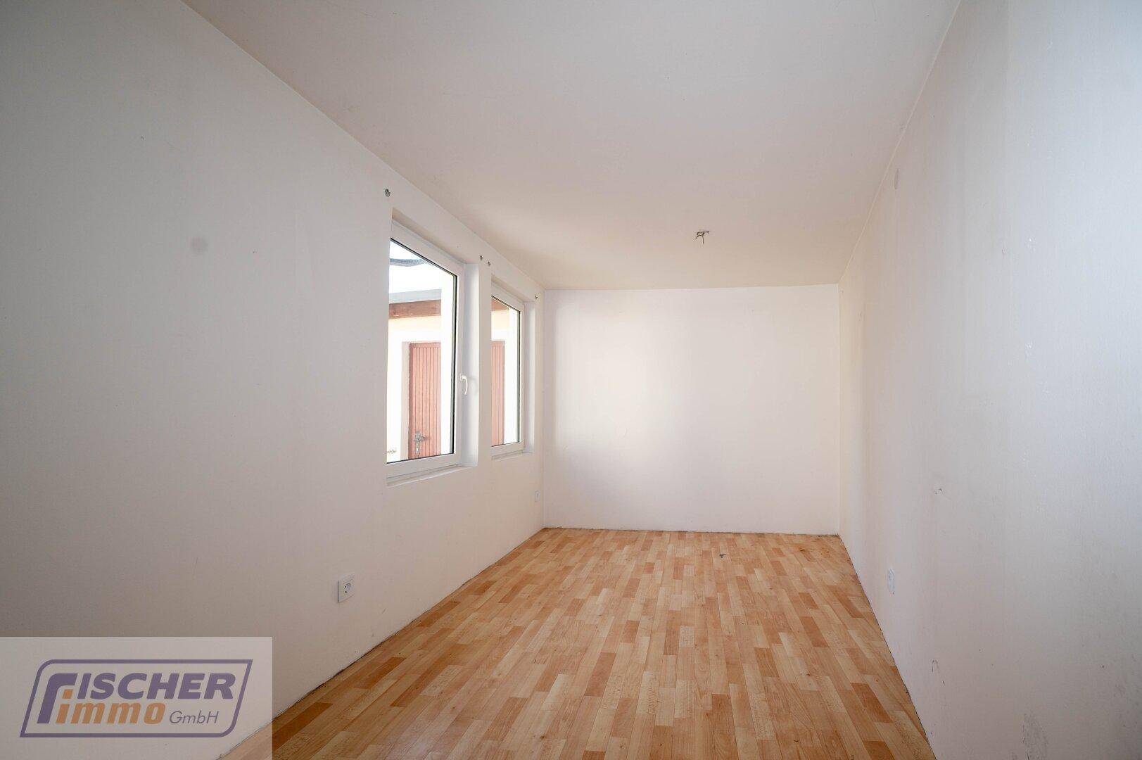 Schlichtes Zimmer mit hellem Laminatboden und mehreren Fenstern für viel Licht.