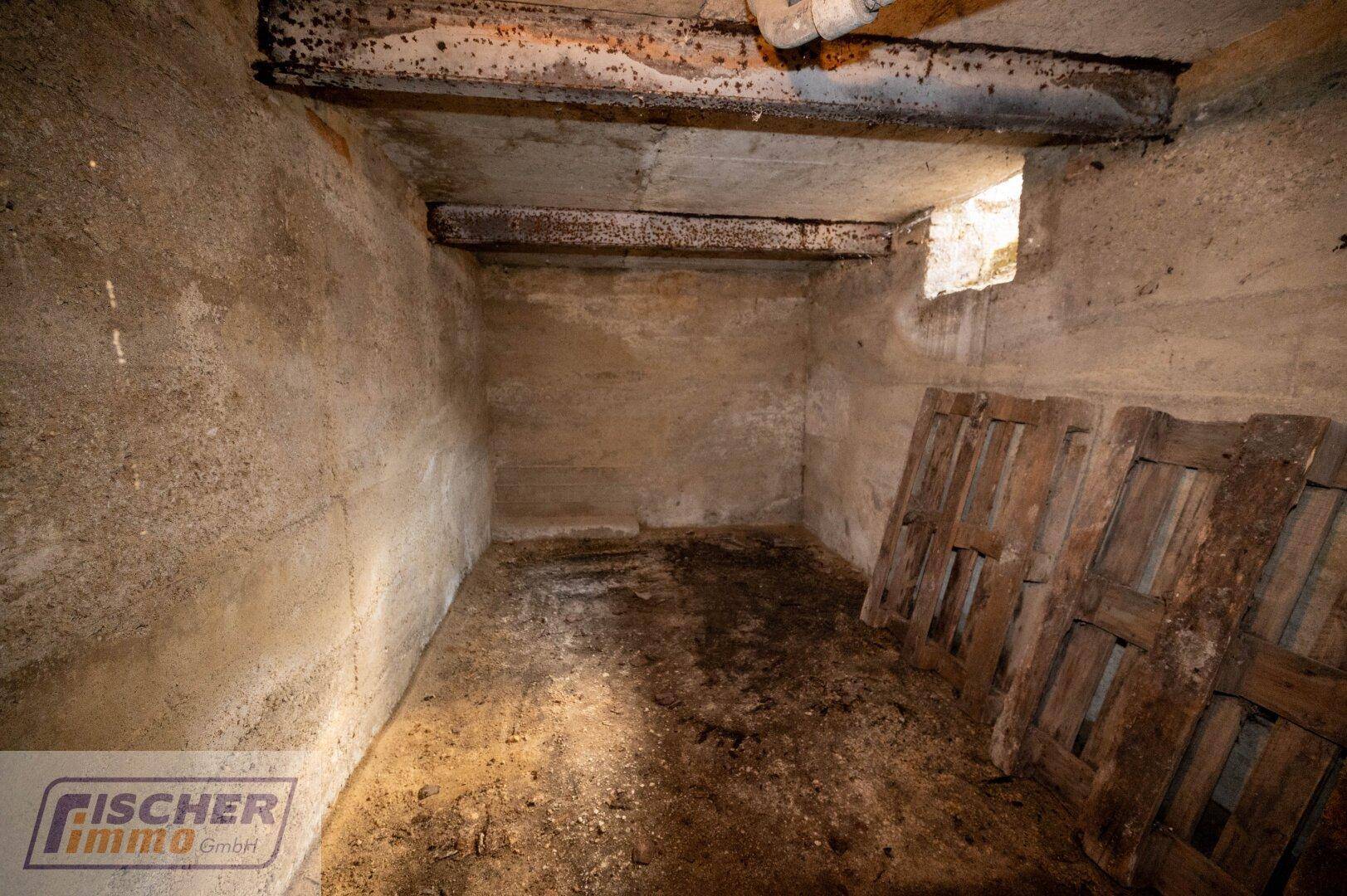 Kellerraum mit Betonwänden, kleinem Fenster und gelagerten Holzpaletten.