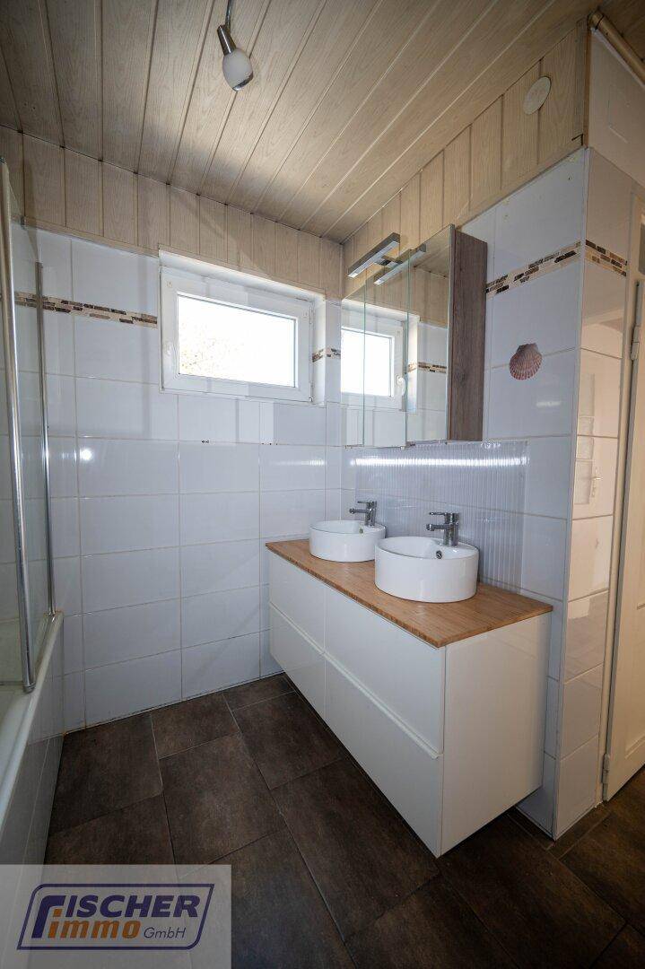 Badezimmer mit zwei Aufsatzwaschbecken auf Holzplatte und Spiegelschrank.