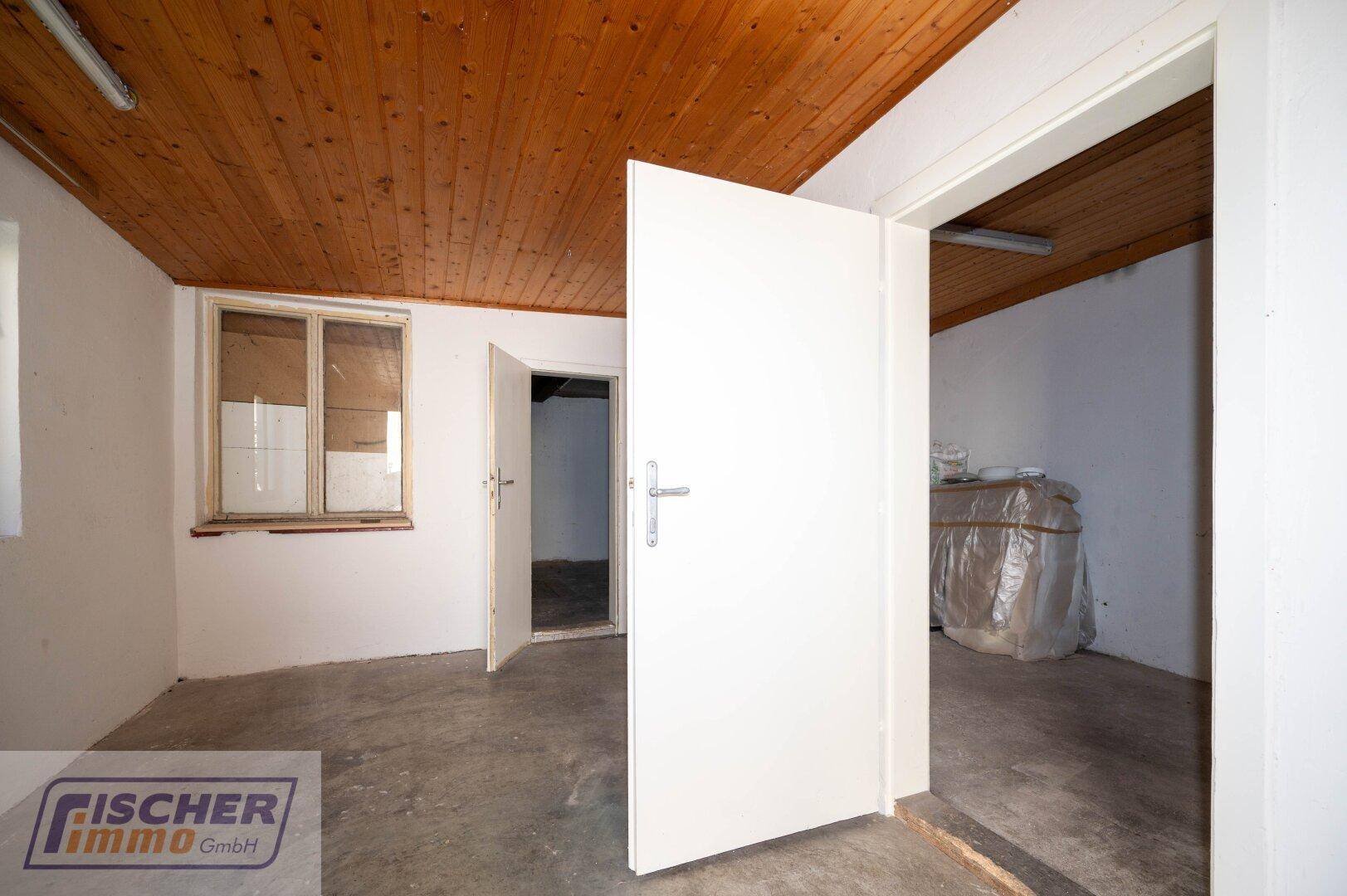 Einfacher Raum mit Holzdecke, Betonboden und einem Fenster, ideal als Abstellraum.