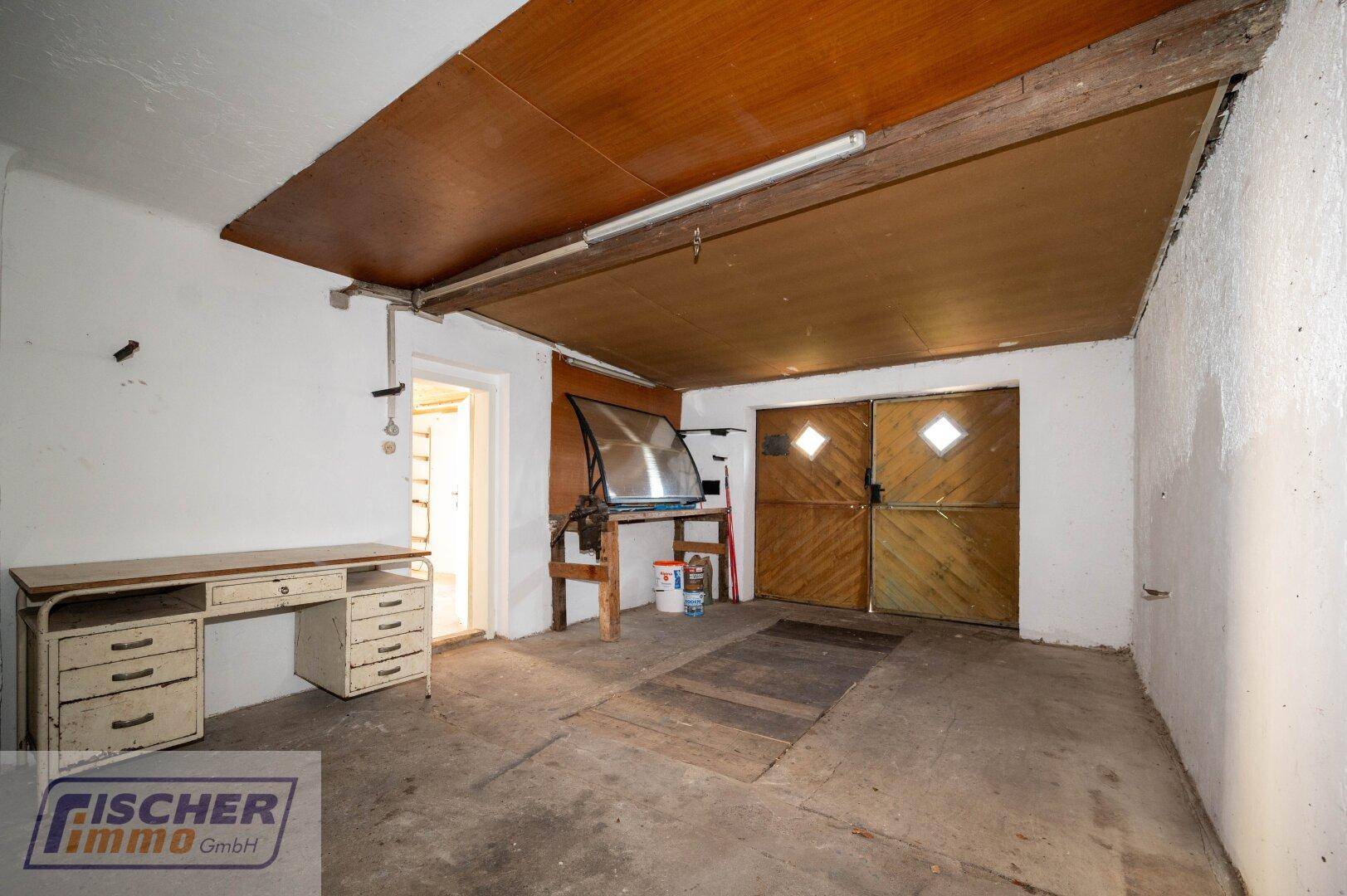 Geräumige Garage oder Werkstatt mit Betonboden, Holzdecke und rustikalen Holztoren.