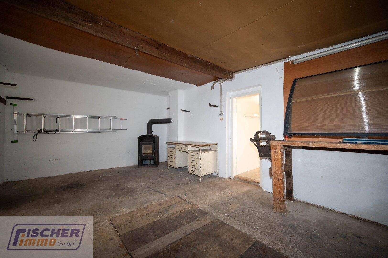 Werkstattbereich in der Garage mit Holzofen, Werkbank und Leiter an der Wand.