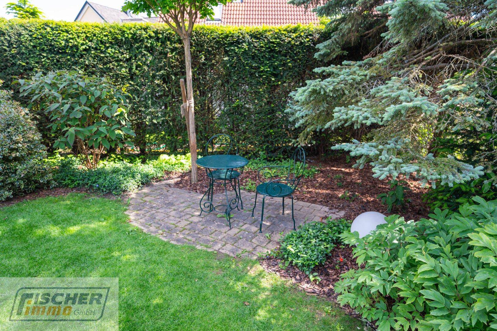 Gemütlicher, kleiner Sitzbereich im Garten mit schmiedeeisernen Möbeln, umgeben von üppigem Grün.