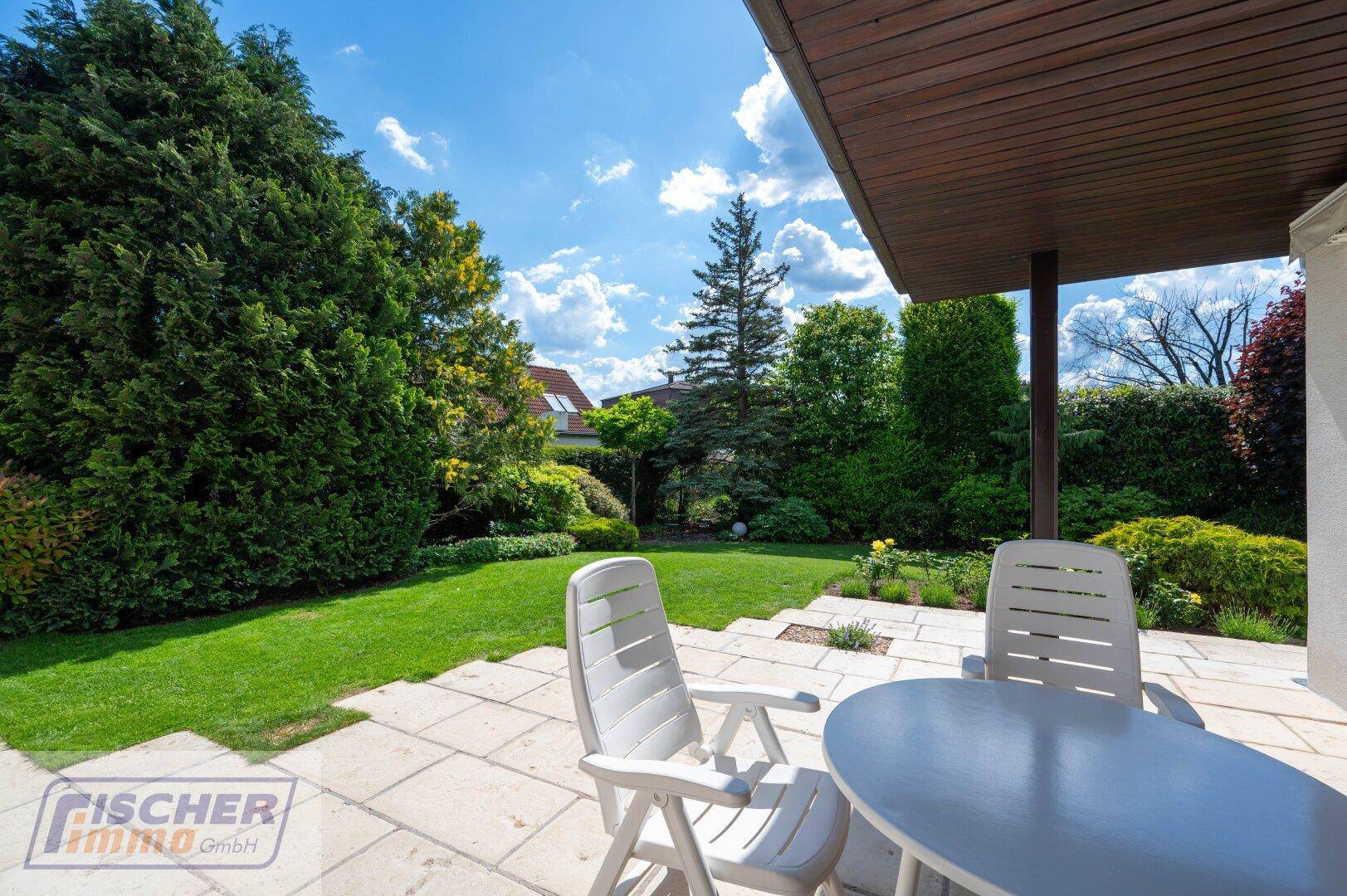 Gemütliche Terrasse mit Gartenmöbeln und Blick auf den gepflegten Garten unter blauem Himmel.