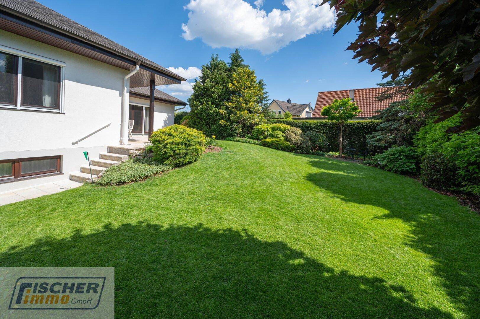 Seitenansicht des Hauses mit einem weitläufigen, sanft abfallenden Rasen und Zugang zum Garten.