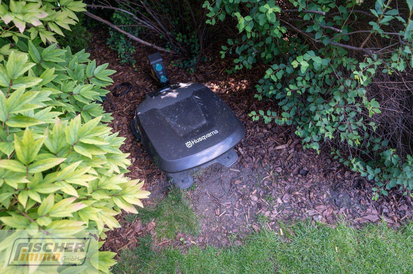 Ein automatischer Rasenmäher im Einsatz zwischen Sträuchern und Pflanzen im gepflegten Gartenbereich.