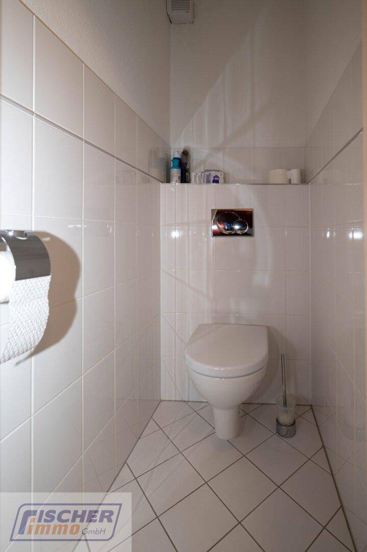 Separates WC mit Wand-WC und weißen Fliesen an Wänden und Boden.