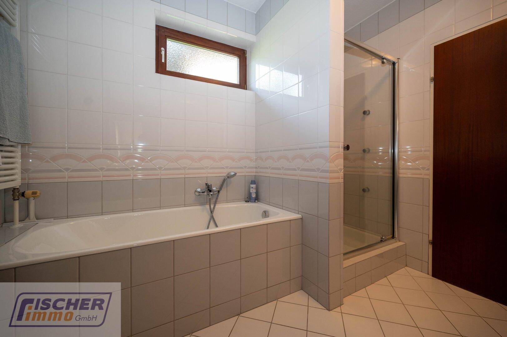 Badezimmer mit Badewanne, Duschkabine und Fliesen in hellen Farbtönen.