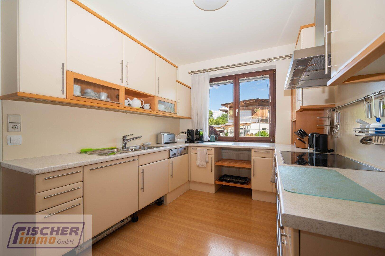 Funktionale Küche mit hellen Holzfronten, Einbaugeräten und Fenster mit Ausblick.