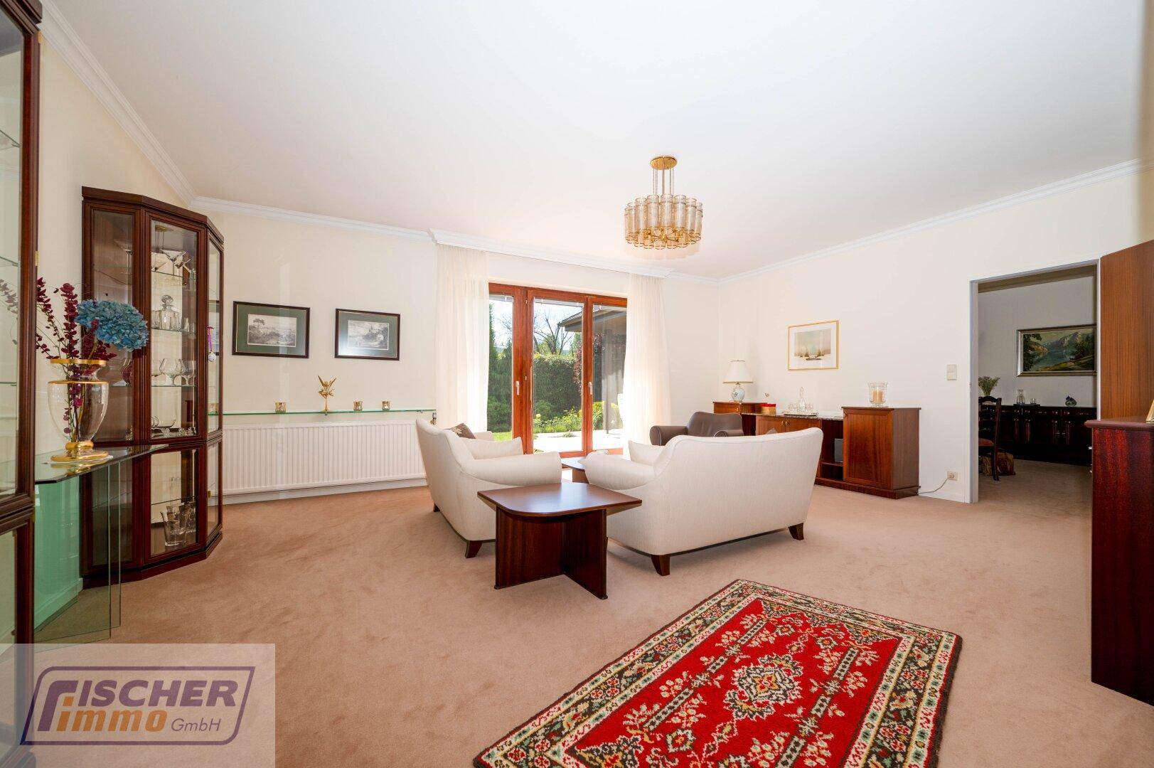 Helles Wohnzimmer mit Teppichboden, bequemen Sofas und Zugang zur Terrasse mit Gartenblick.