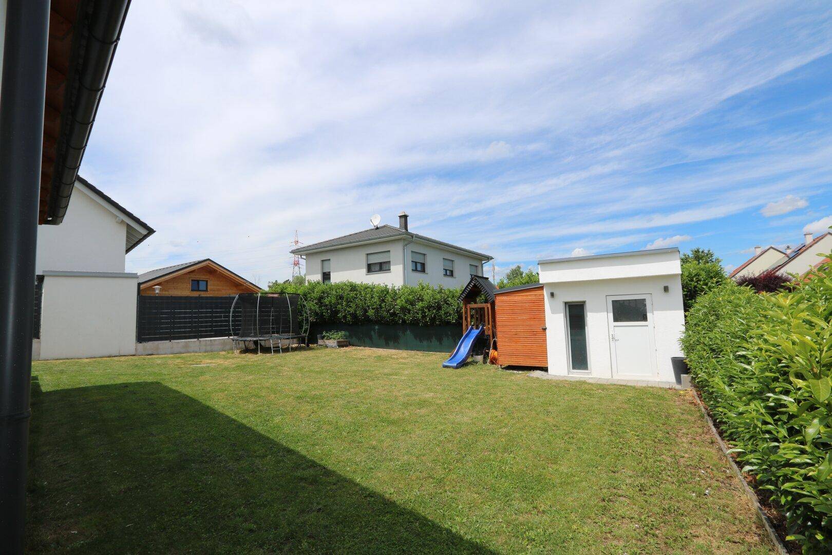 Geräumiger Garten mit Rasenfläche, Trampolin, Spielhaus mit Rutsche und einem kleinen Geräteschuppen.