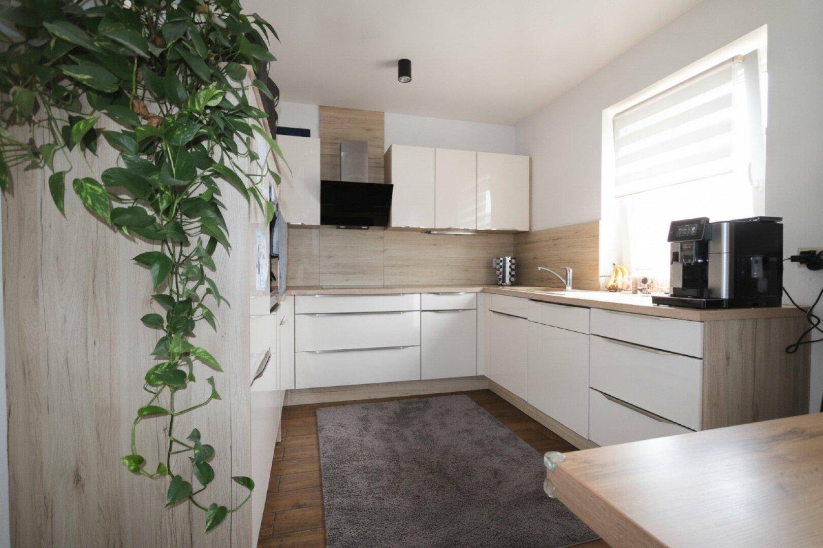 Moderne Küche mit weißen Hochglanzfronten, Holzakzenten und Fenster.