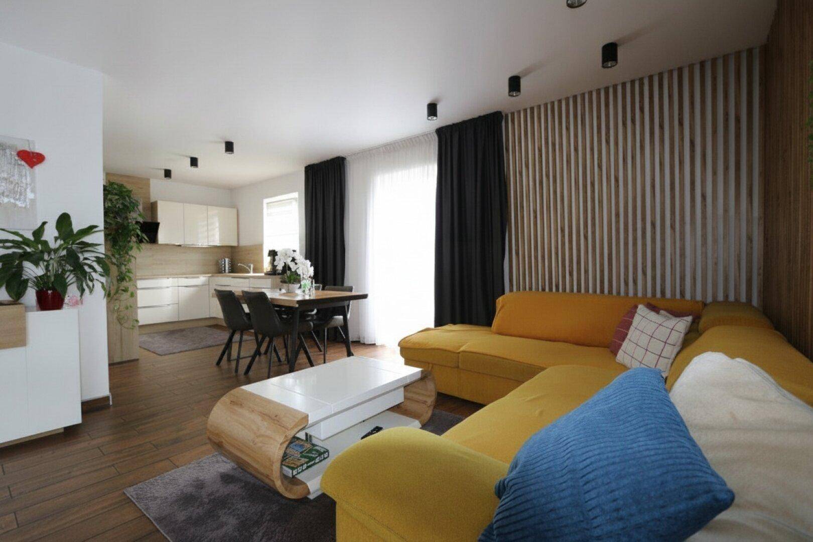 Heller offener Wohnbereich mit gelbem Sofa, Essbereich und moderner Küche.