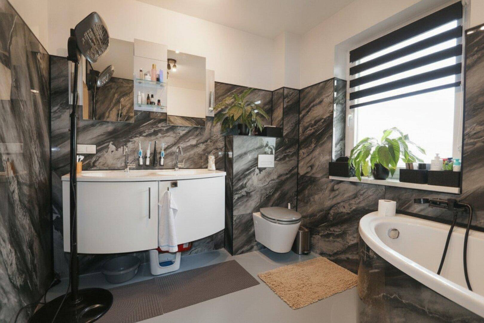 Modernes Badezimmer mit dunklen Marmorfliesen, Badewanne und Fenster.