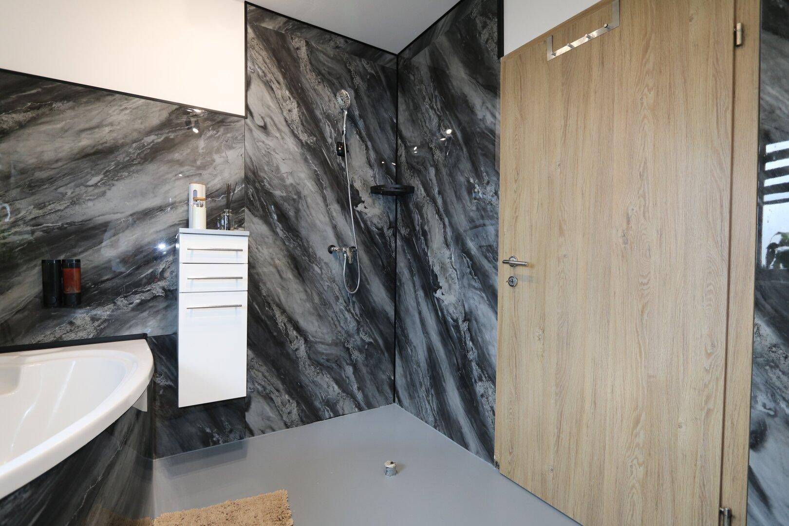 Modernes Badezimmer mit großer Dusche, dunklen Marmorfliesen und Holztür.