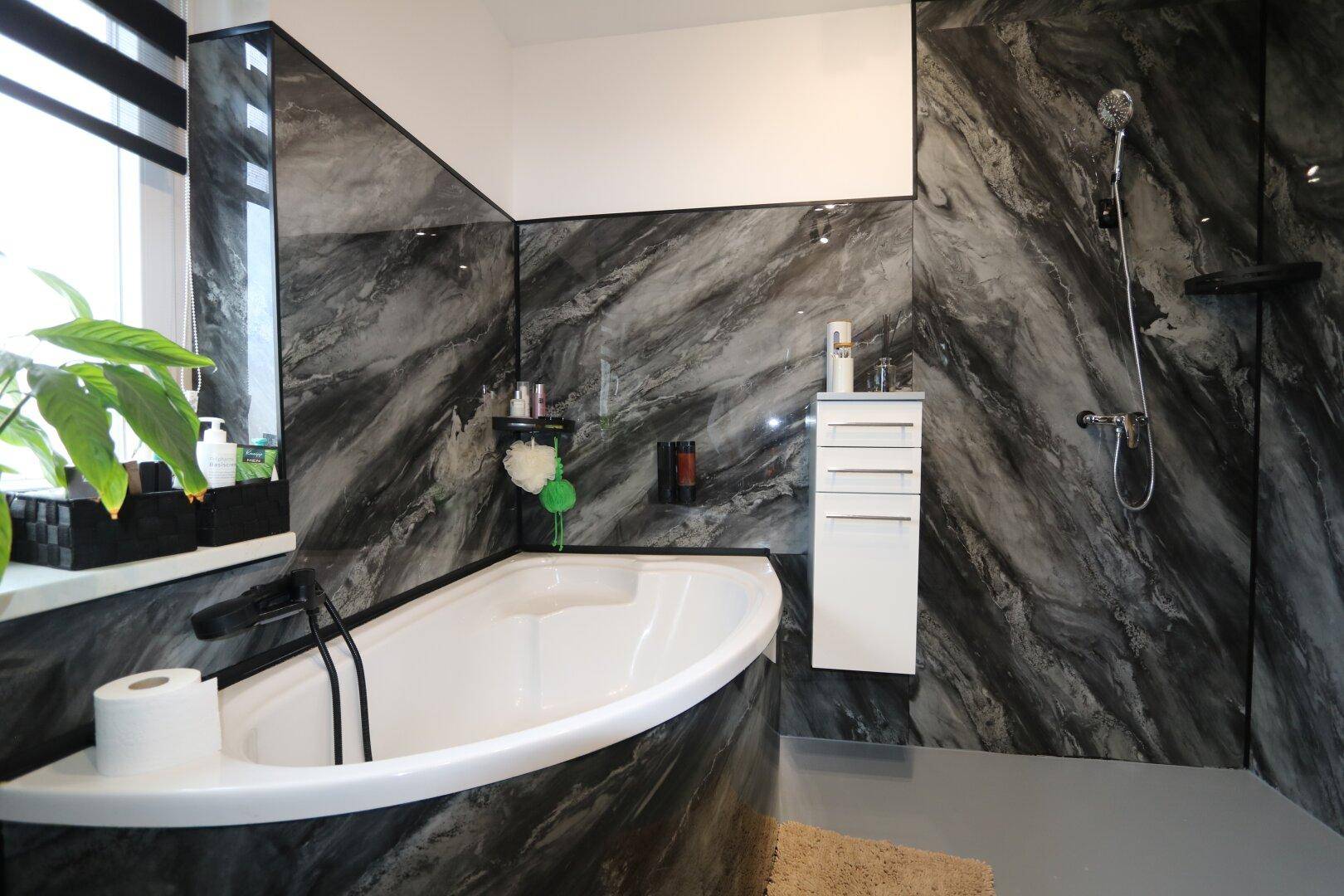 Modernes Badezimmer mit Badewanne, Dusche und dunklen Marmorfliesen.