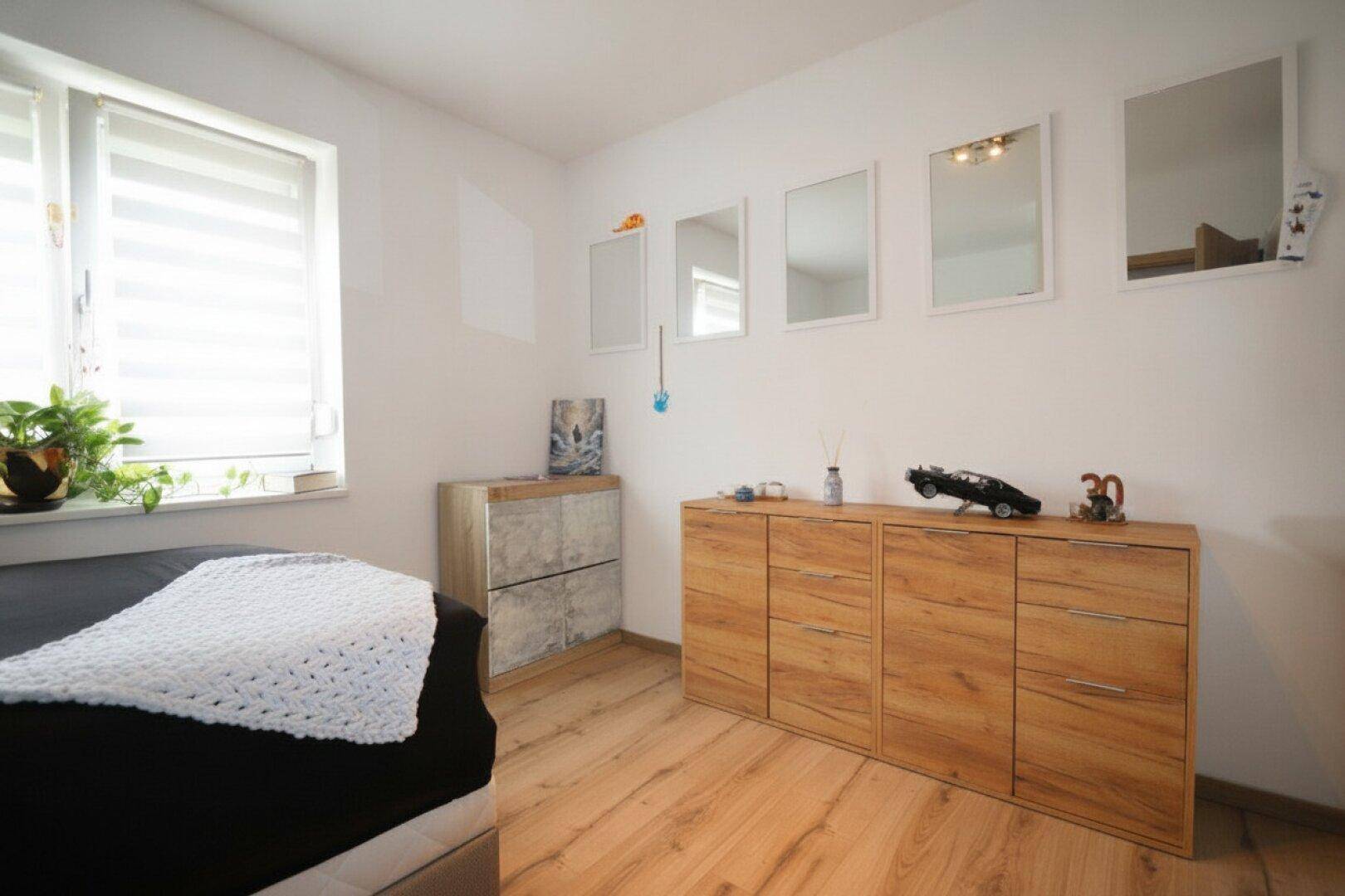 Schlafzimmer mit Holzboden, Kommode und mehreren Wandspiegeln.