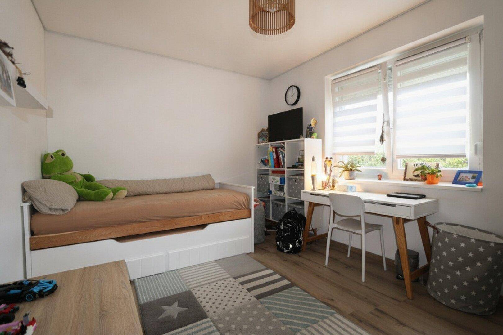 Kinderzimmer mit Bett, Schreibtisch, Regal und Laminatboden.