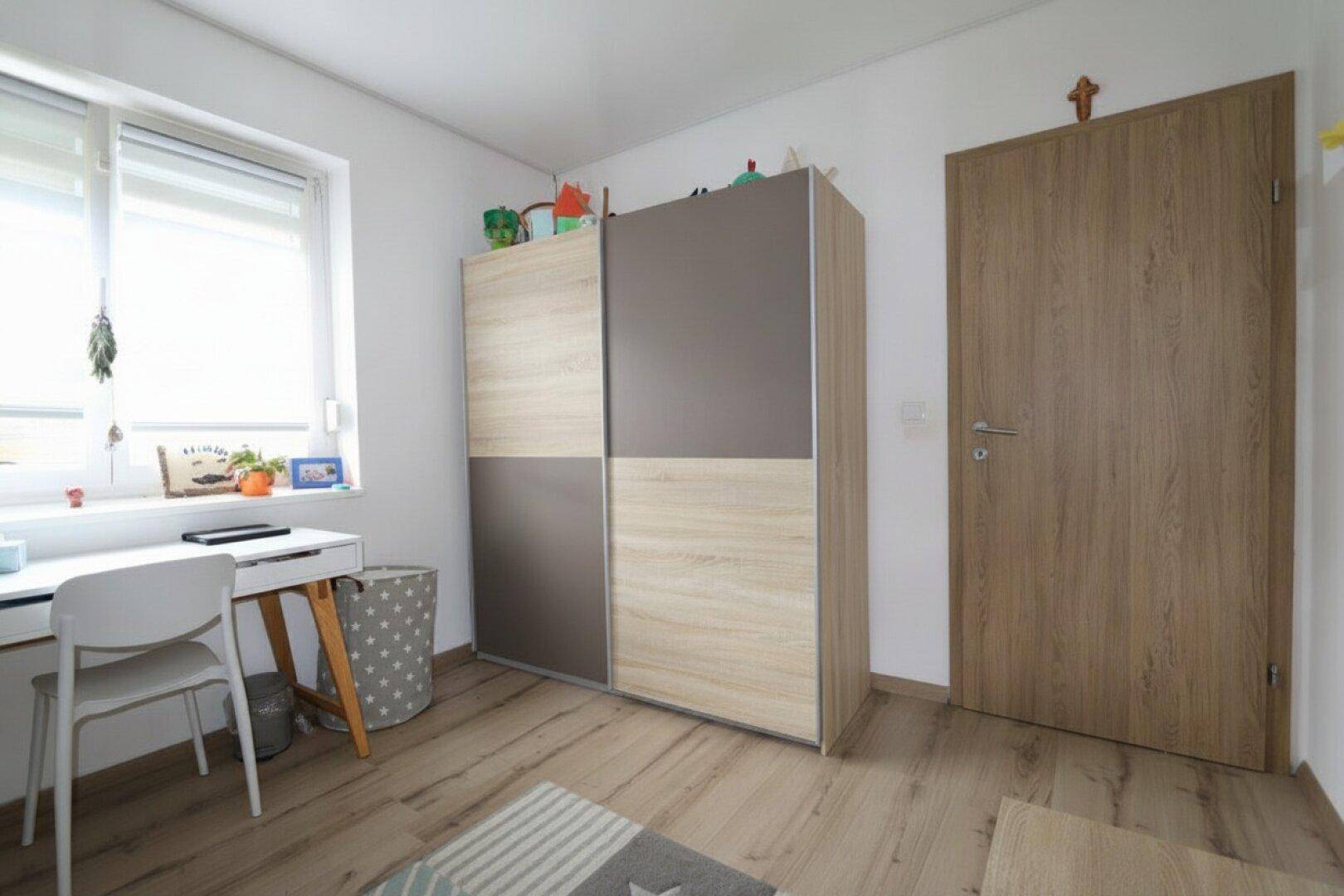 Kinderzimmer mit Schreibtisch, Kleiderschrank und Laminatboden.