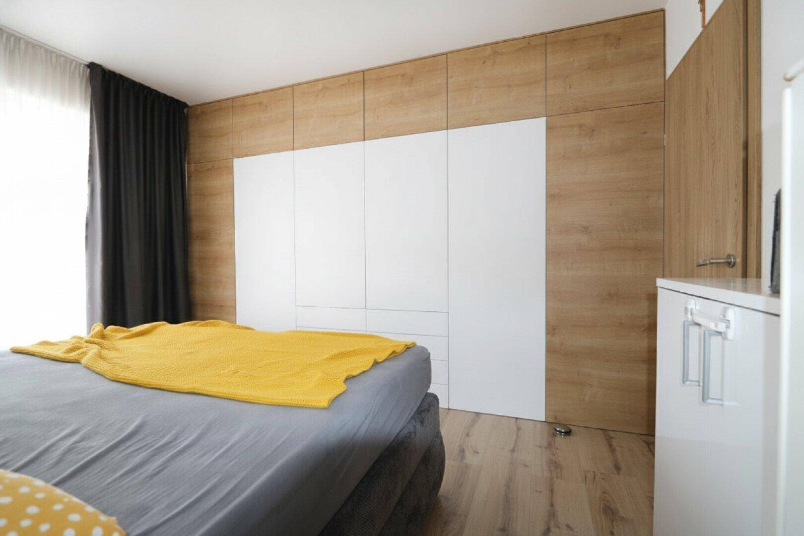 Schlafzimmer mit integriertem Kleiderschrank, Holzwandverkleidung und Laminatboden.