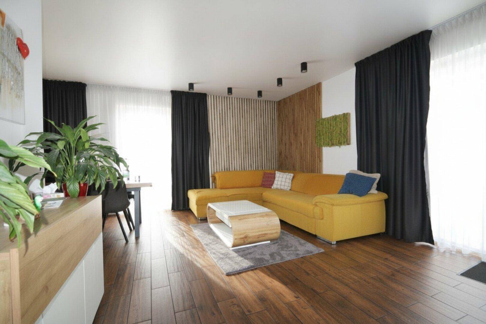 Helles Wohnzimmer mit gelbem Ecksofa, Holzboden und dekorativer Wandverkleidung.