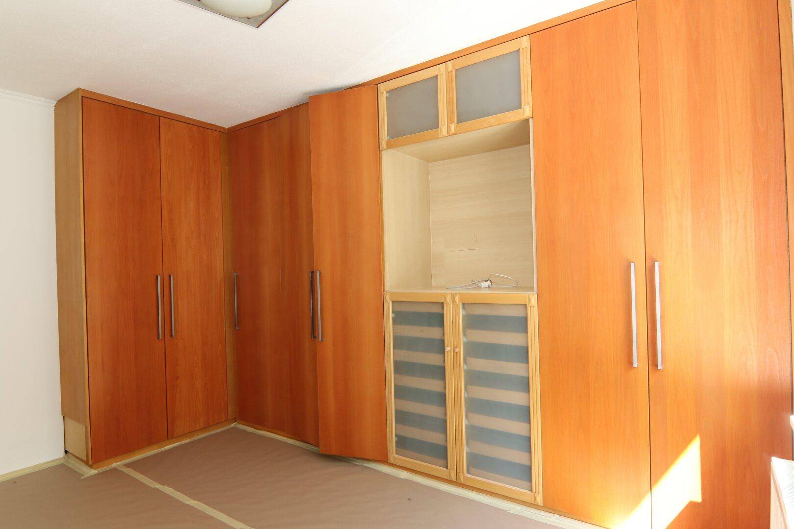 Geräumiges Zimmer mit maßgefertigten Holzeinbauschränken, die sich über eine Ecke erstrecken und viel Stauraum bieten.
