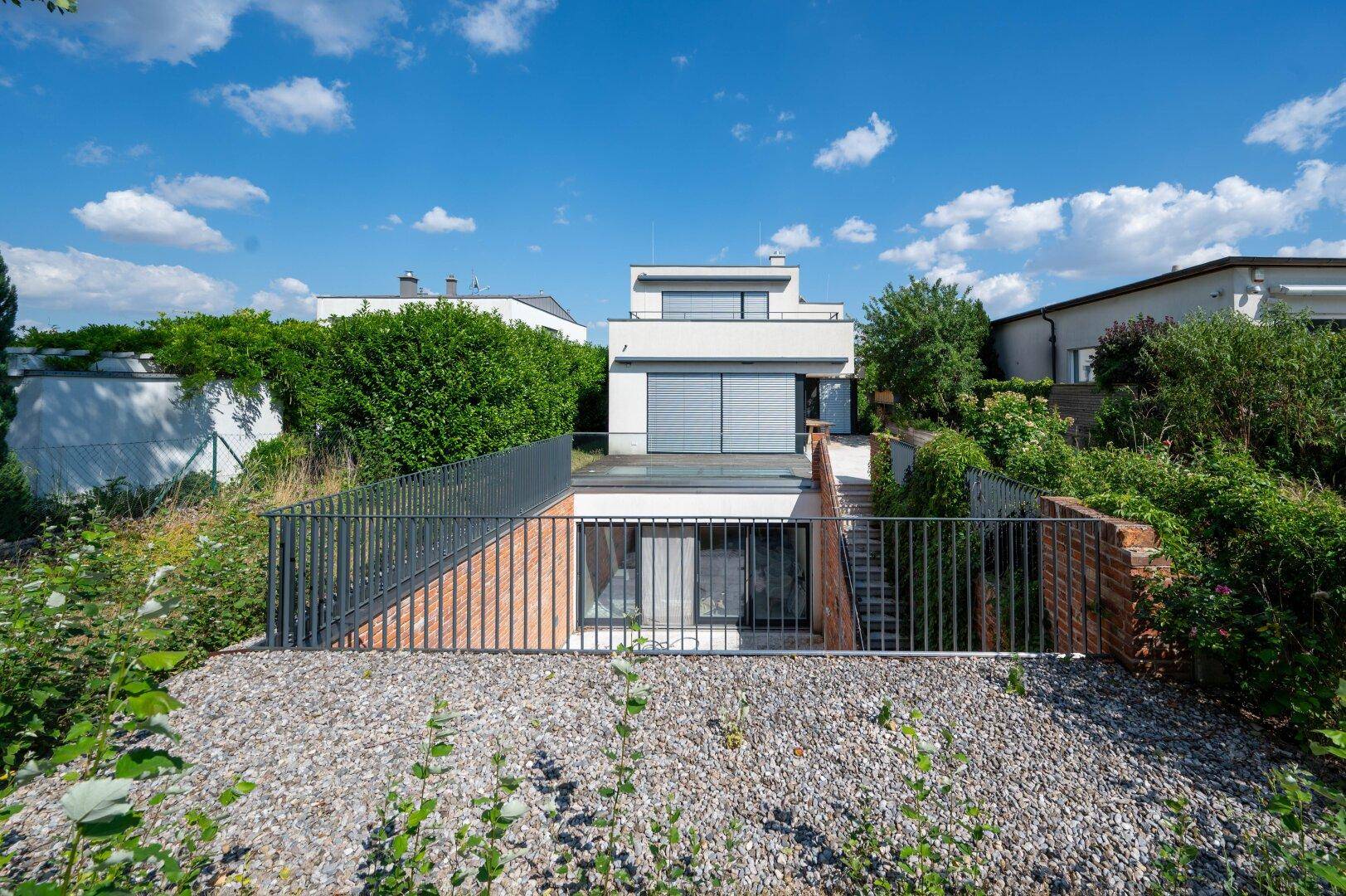 Moderne Architektur mit weißer Fassade und großen Fenstern, umgeben von viel Grün.