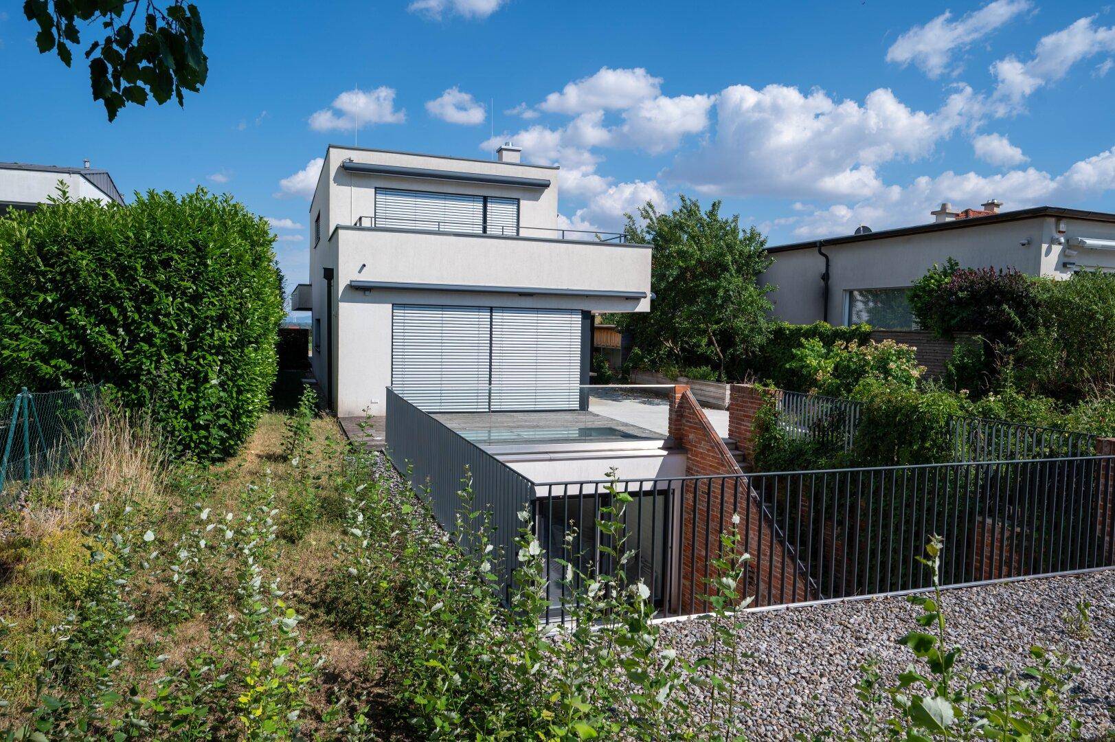 Zeitgenössisches Wohnhaus mit weißer Fassade und Balkon, eingebettet in eine grüne Umgebung.