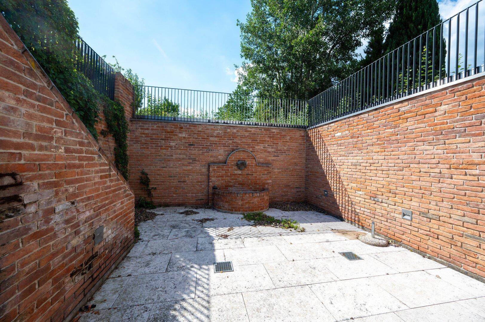 Gemütlicher Innenhof mit Steinplatten und einem dekorativen Brunnen an der Ziegelwand.