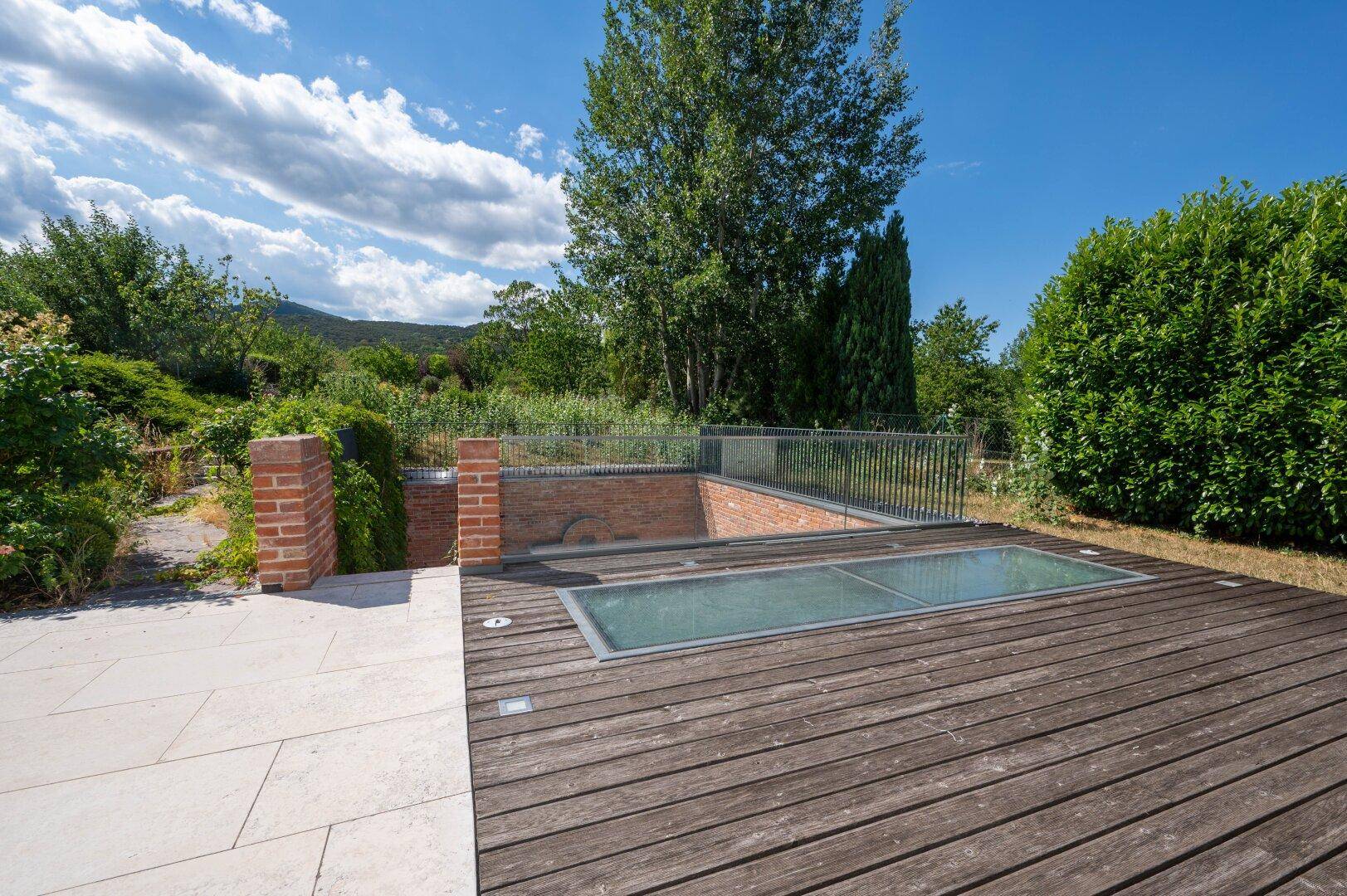 Terrasse mit Holzboden und integrierten Glasflächen, umgeben von üppigem Grün.