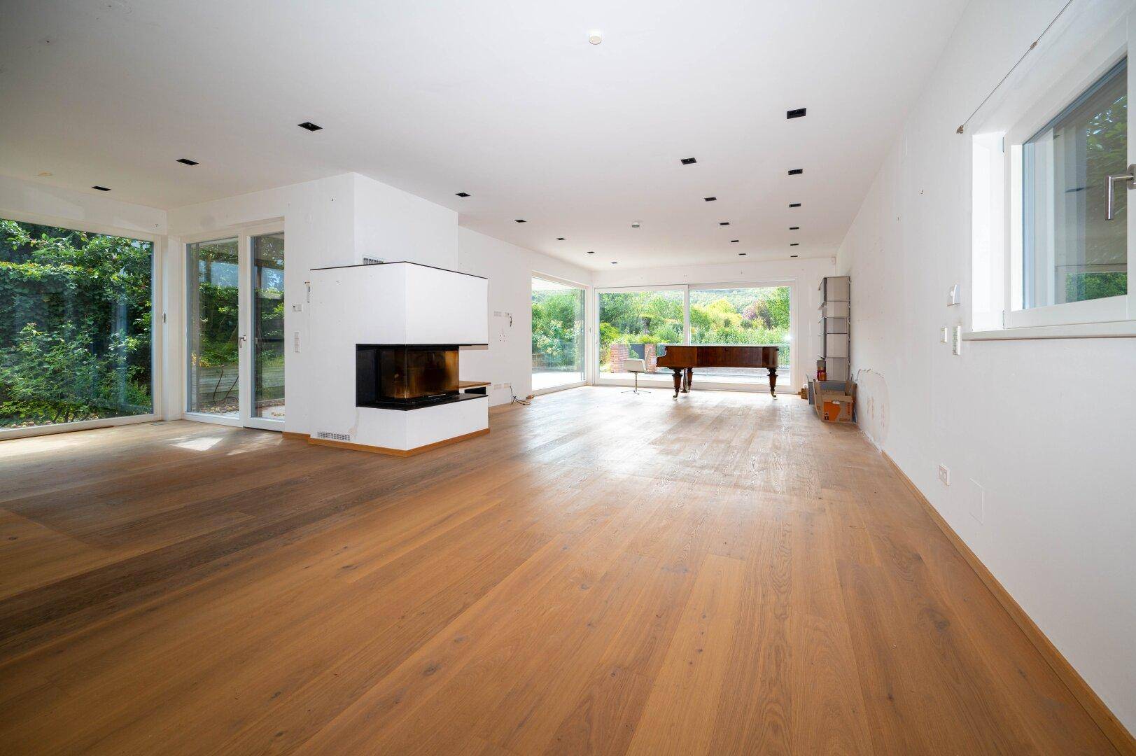 Großzügiges Wohnzimmer mit Holzboden, modernem Kamin und bodentiefen Fenstern zum Garten.
