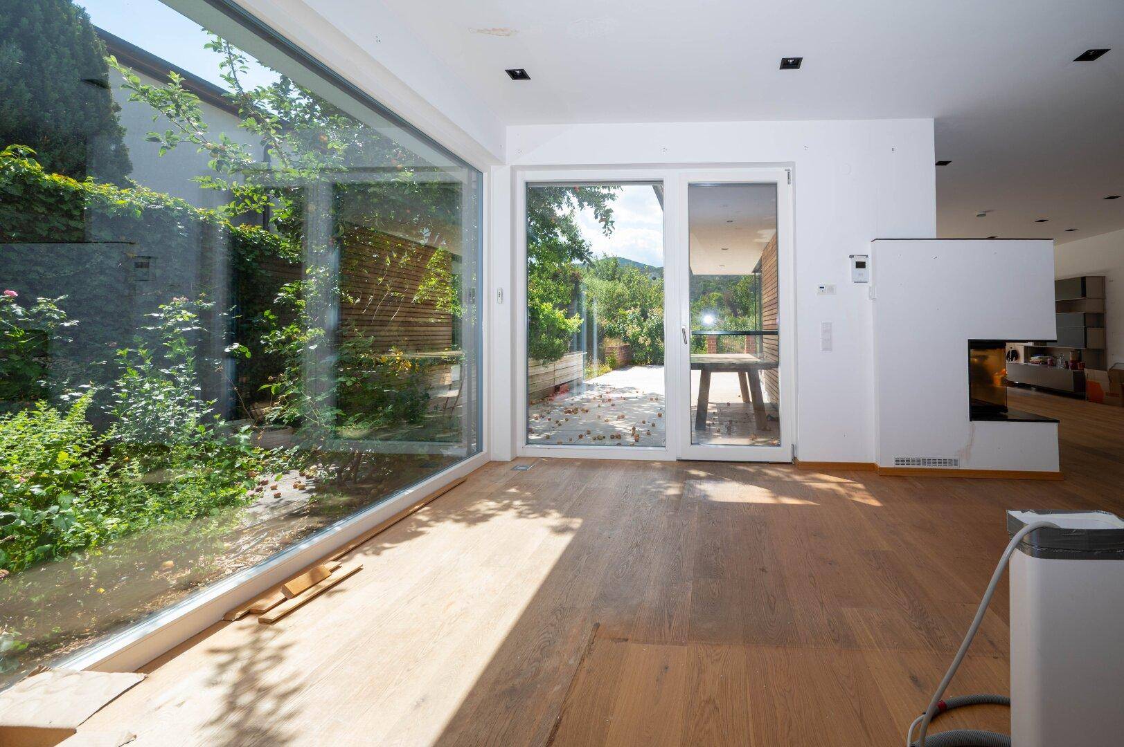 Lichtdurchfluteter Raum mit großen Glasfronten und Holzboden, der einen direkten Blick ins Grüne bietet.