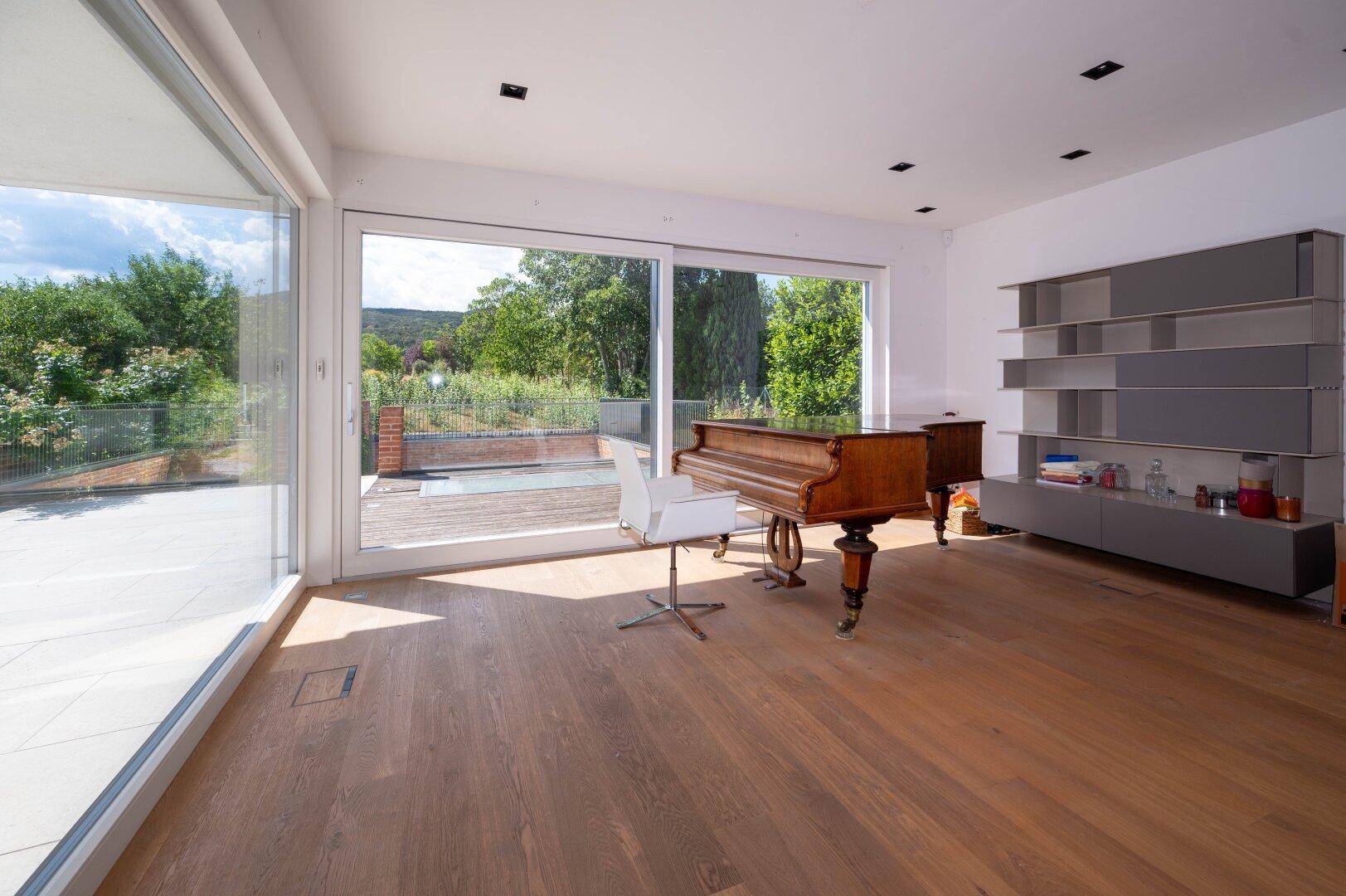 Geräumiges Wohnzimmer mit Holzboden, großen Schiebetüren zur Terrasse und weitem Blick ins Grüne.