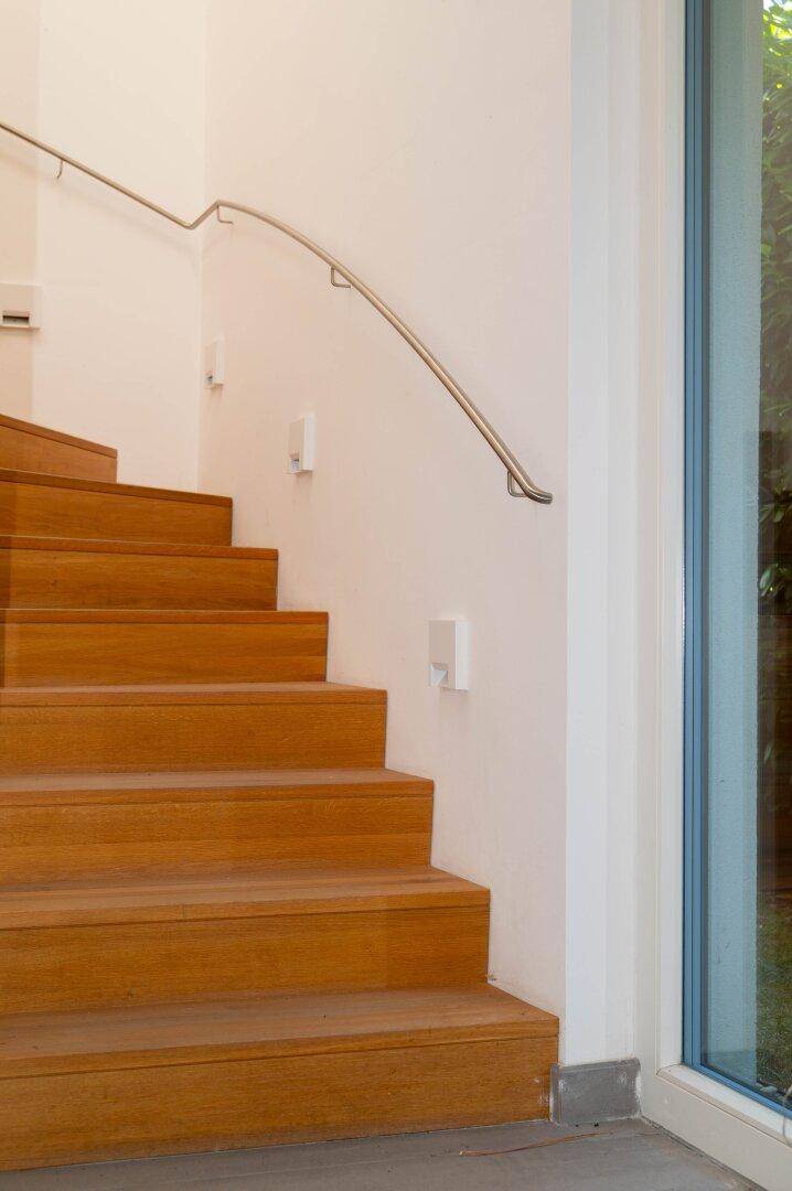 Elegante Holztreppe mit modernem Metallgeländer neben einem großen Fenster.