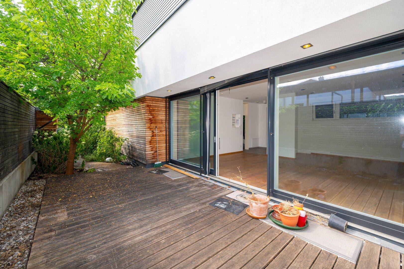 Holzterrasse mit Baum und großen Glasschiebetüren, die den Übergang zum Innenbereich schaffen.