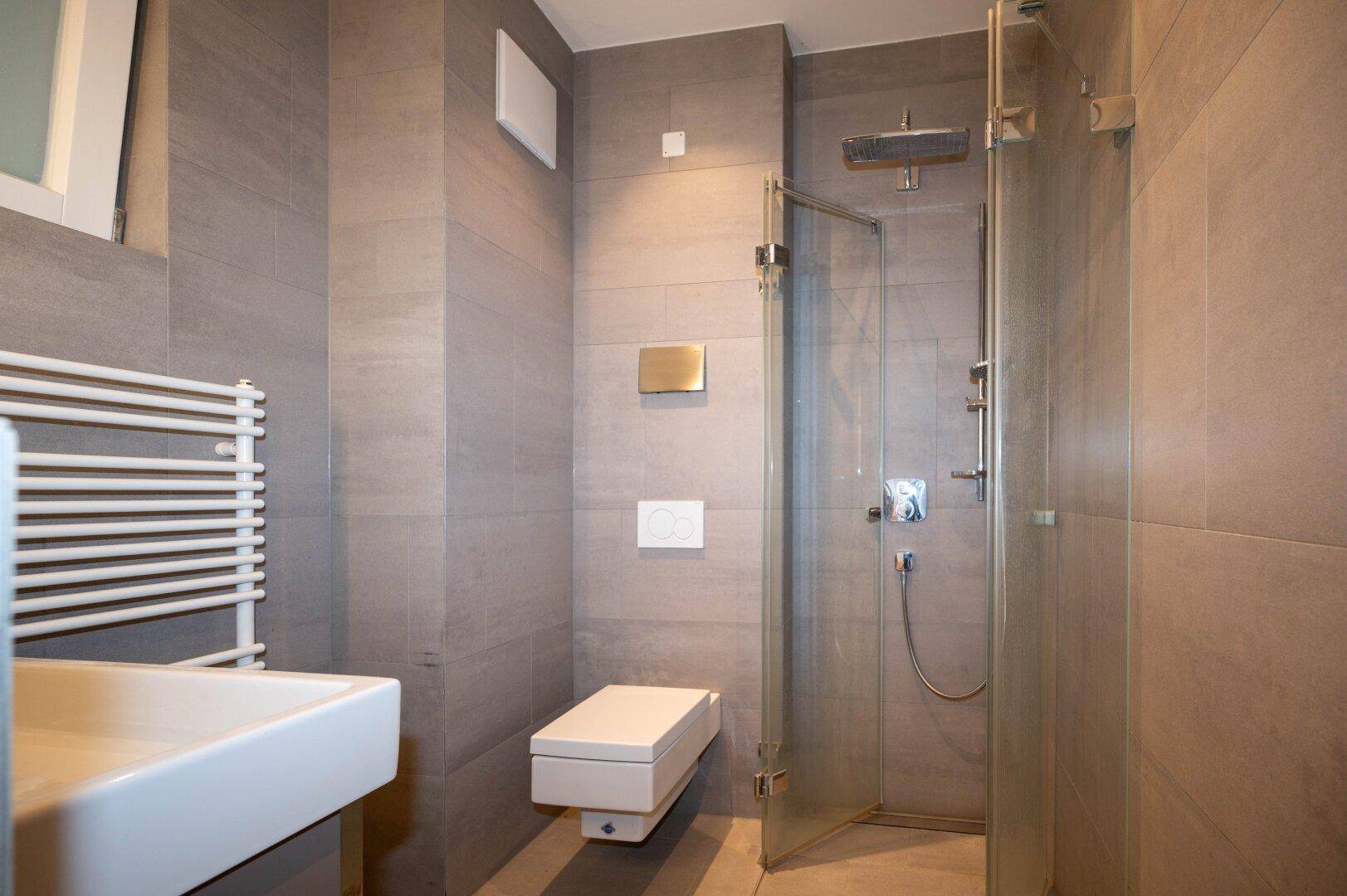 Modernes Badezimmer mit grauen Fliesen, bodengleicher Dusche und beheiztem Handtuchhalter.
